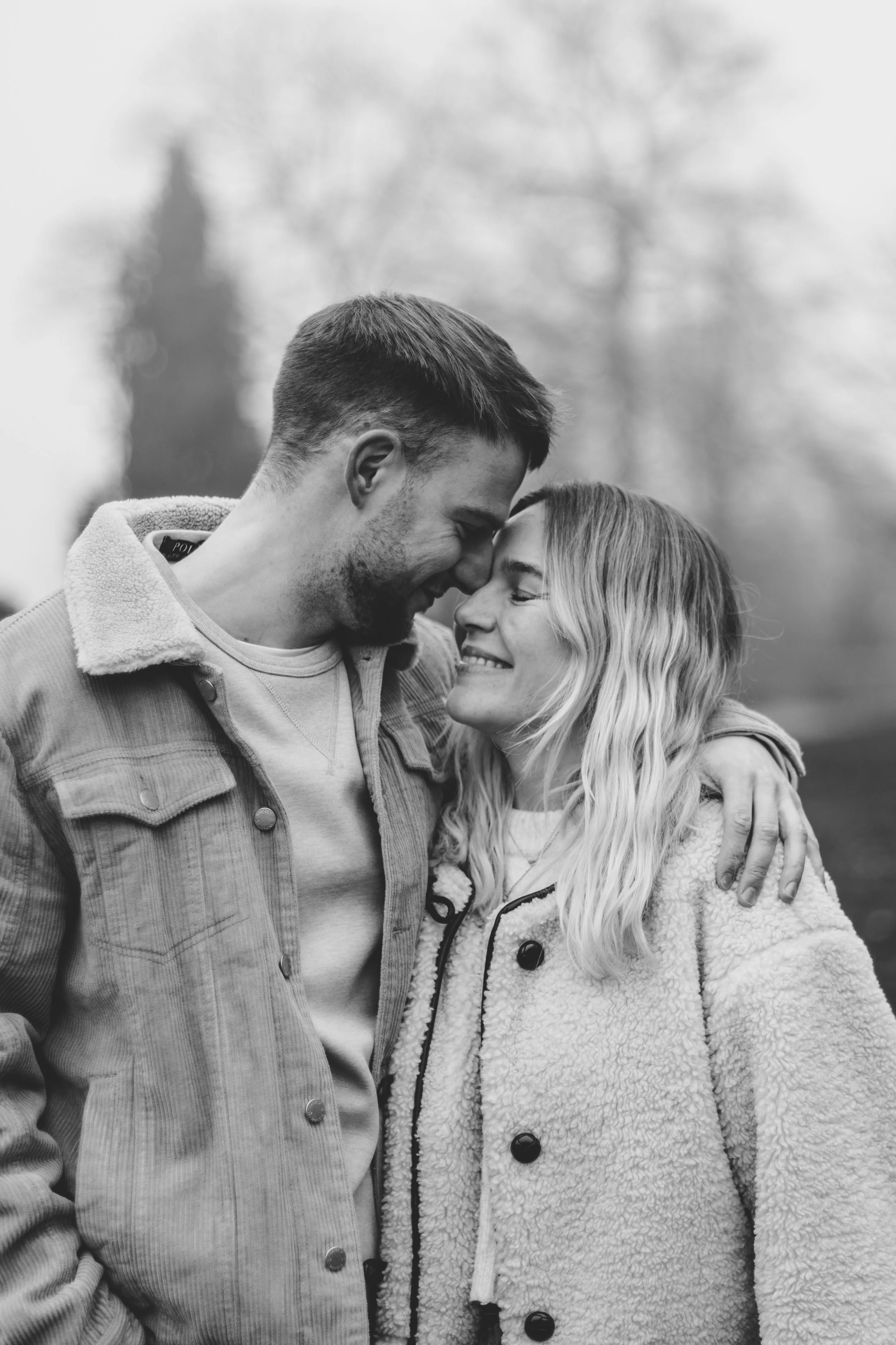 Black and white photo of a couple embracing outdoors, smiling at each other.