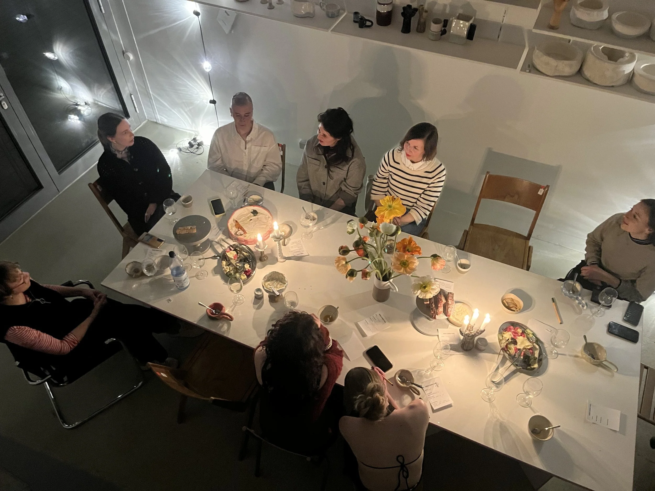 Menschen sitzen um einen Esstisch bei einer Geburtstagsfeier. Auf dem Tisch stehen Blumen, Kerzen, Getränke und Essen.