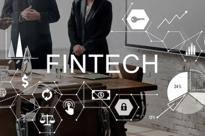 Business people in suits with their hands clasped, standing in a modern office with a large digital overlay graph display that reads 'FINTECH'. The overlay includes icons of a key, graph lines, bar charts, a lock, and currency symbols, representing financial technology concepts.