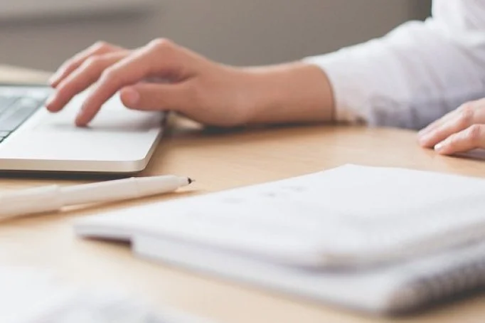 Person using a laptop at a desk with papers and a pen nearby.