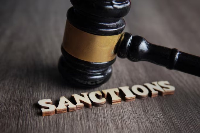 A judge's gavel resting on a wooden surface with the word 'SANCTIONS' spelled out in wooden letters beneath it.
