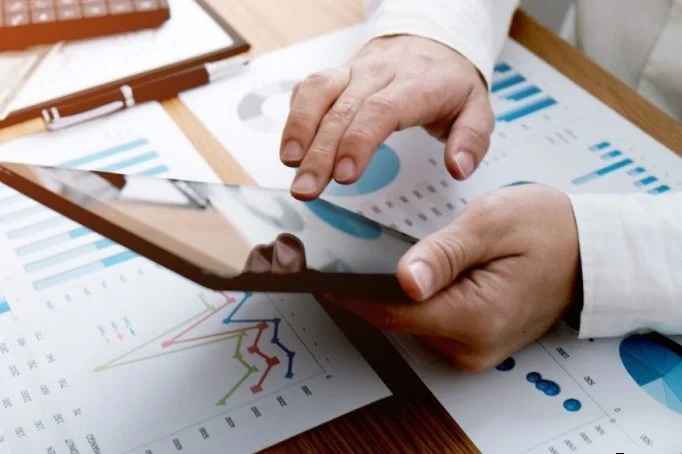 Person using a tablet on a desk with financial charts and graphs.