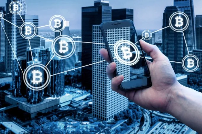 A person holding a smartphone in front of a cityscape with digital Bitcoin symbols and lines representing cryptocurrency connections.