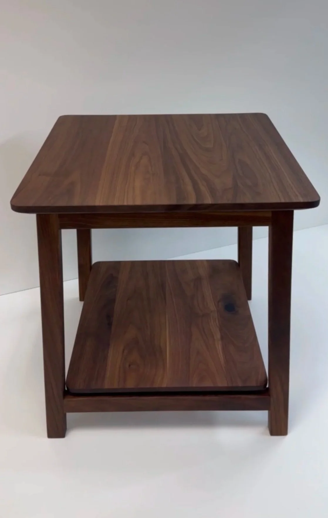Wooden end table with lower shelf on white background.