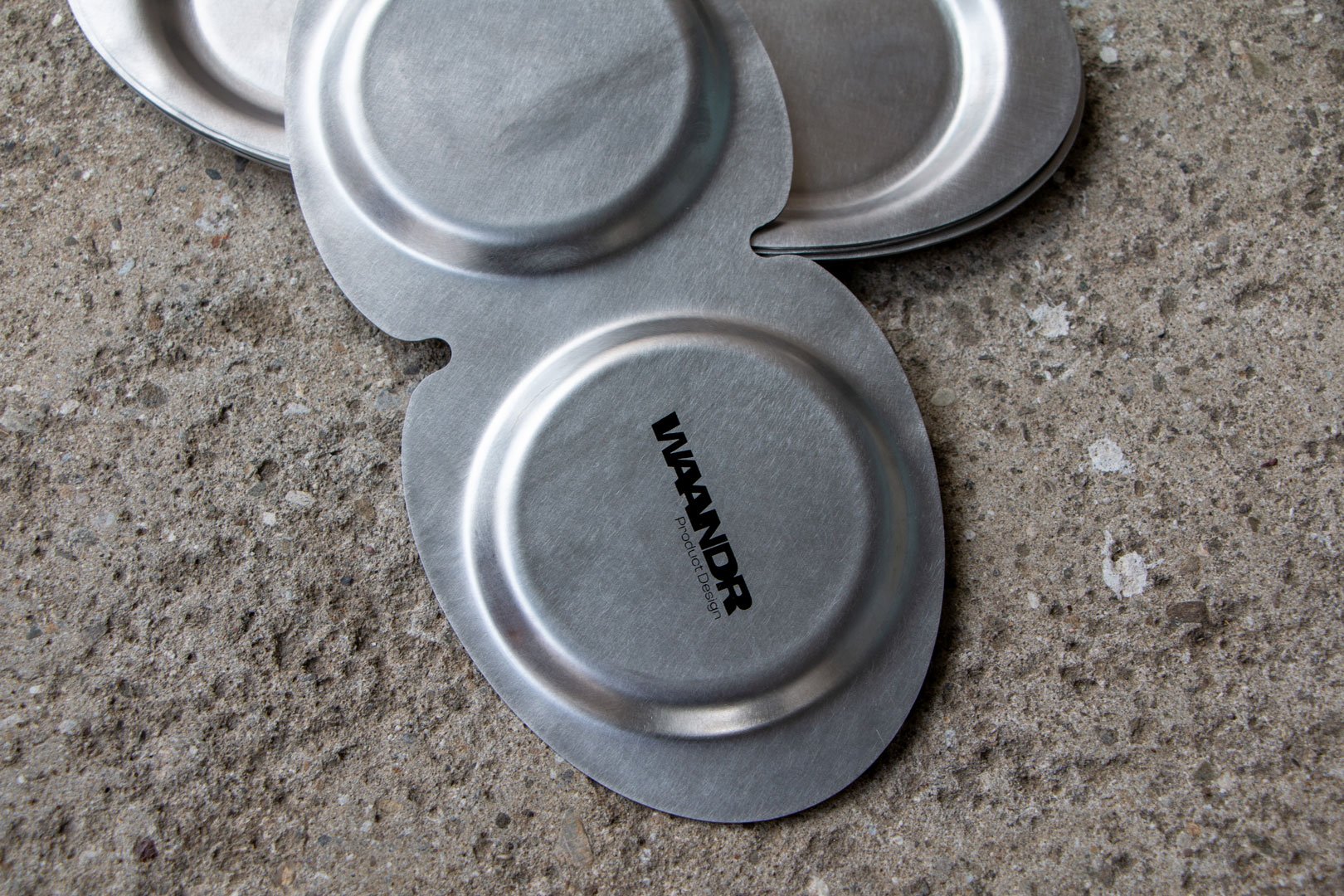 Mehrere runde Metalldeckel oder -deckel auf einer Steinoberfläche, einer mit dem Text "WANDR" und "Product Design".