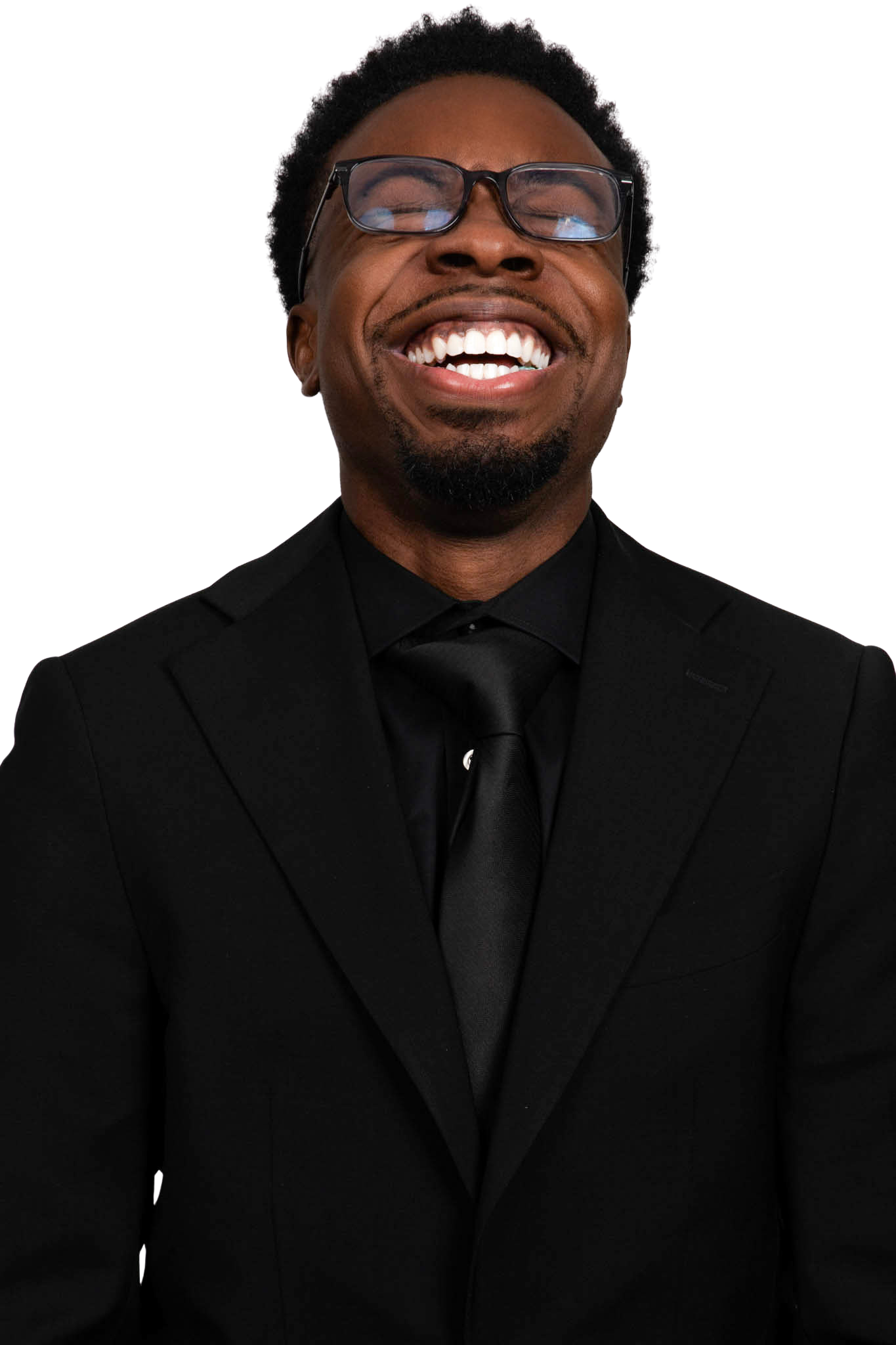 Smiling man wearing a black tuxedo laughing with head tilted upward, and an off-white background