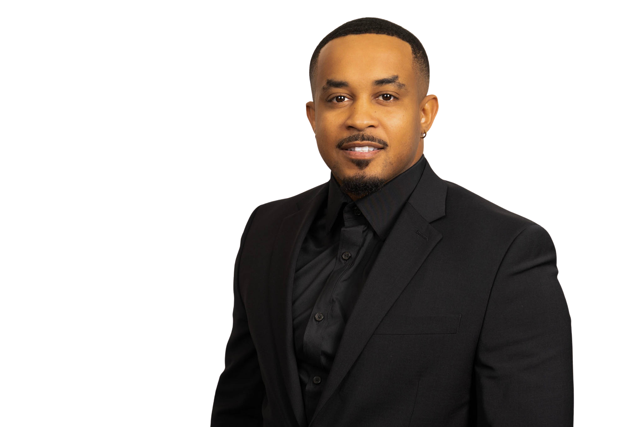 Man in a black suit and black shirt with black tie against an off-white background