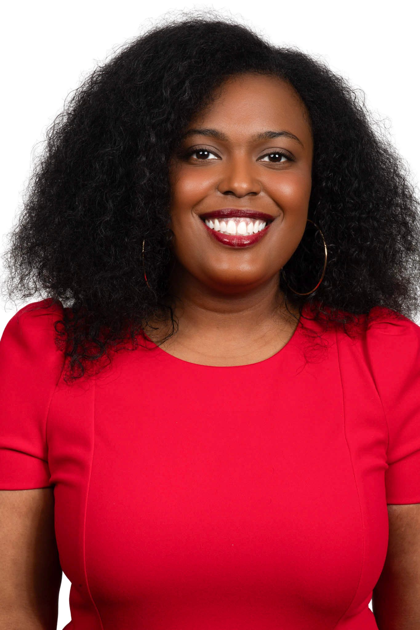 A smiling woman with dark hair wearing a red dress and hoop earrings.