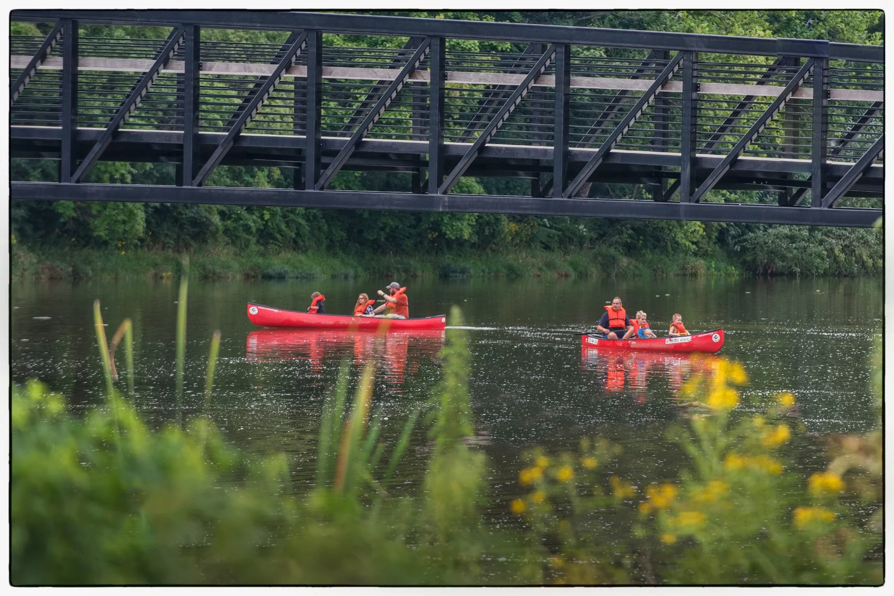 Image contains people kayaking under a bridge in the river.
