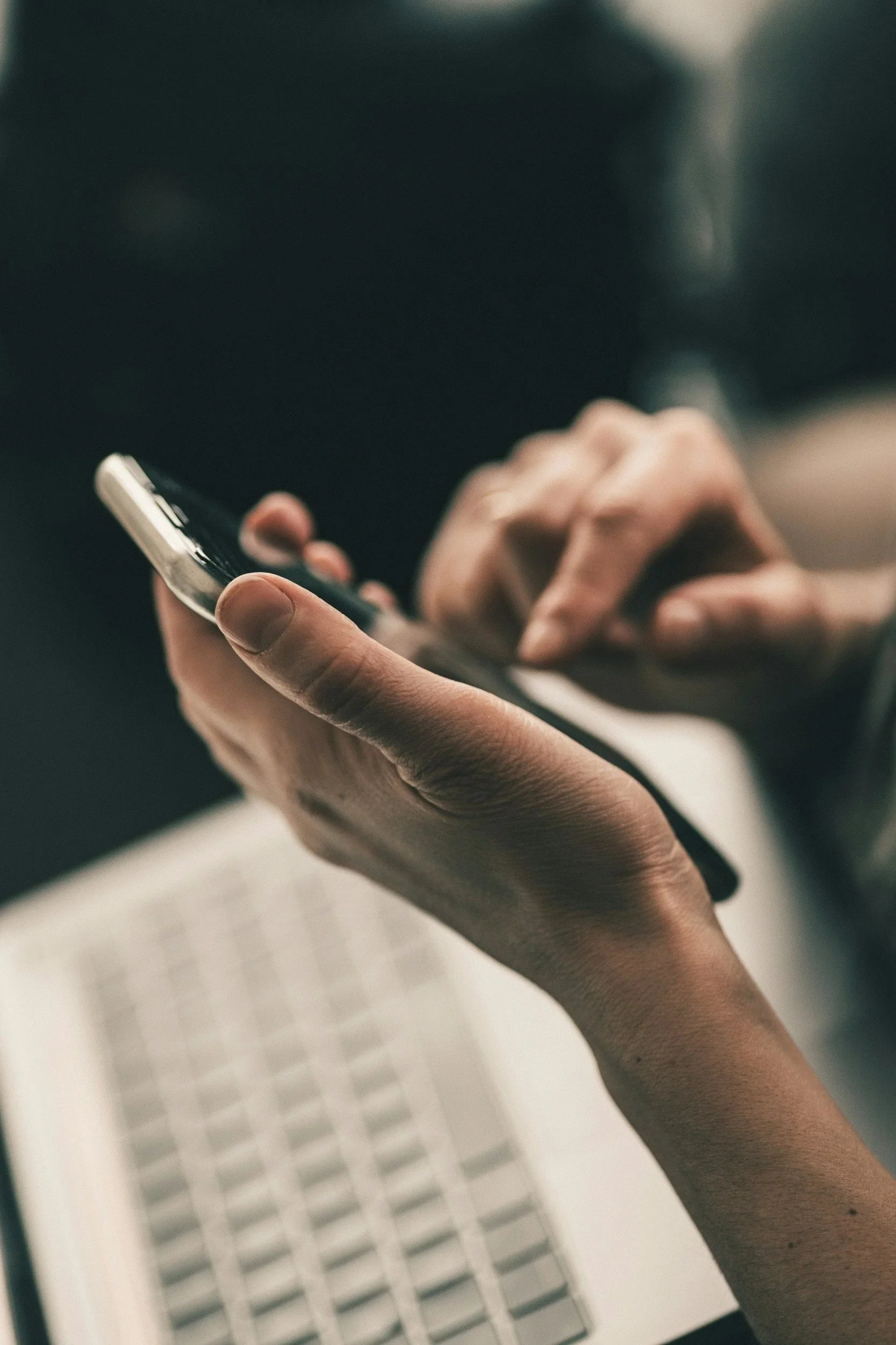Close-up of a person's hand holding a smartphone, with a blurred background featuring a white louvered door or window.