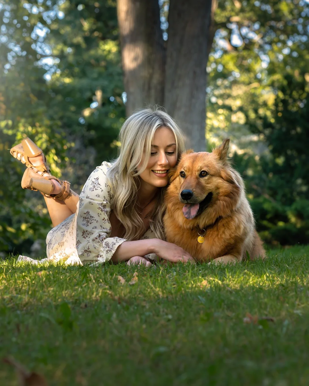 A woman with blonde hair lying on her stomach in a park, hugging a golden retriever dog.