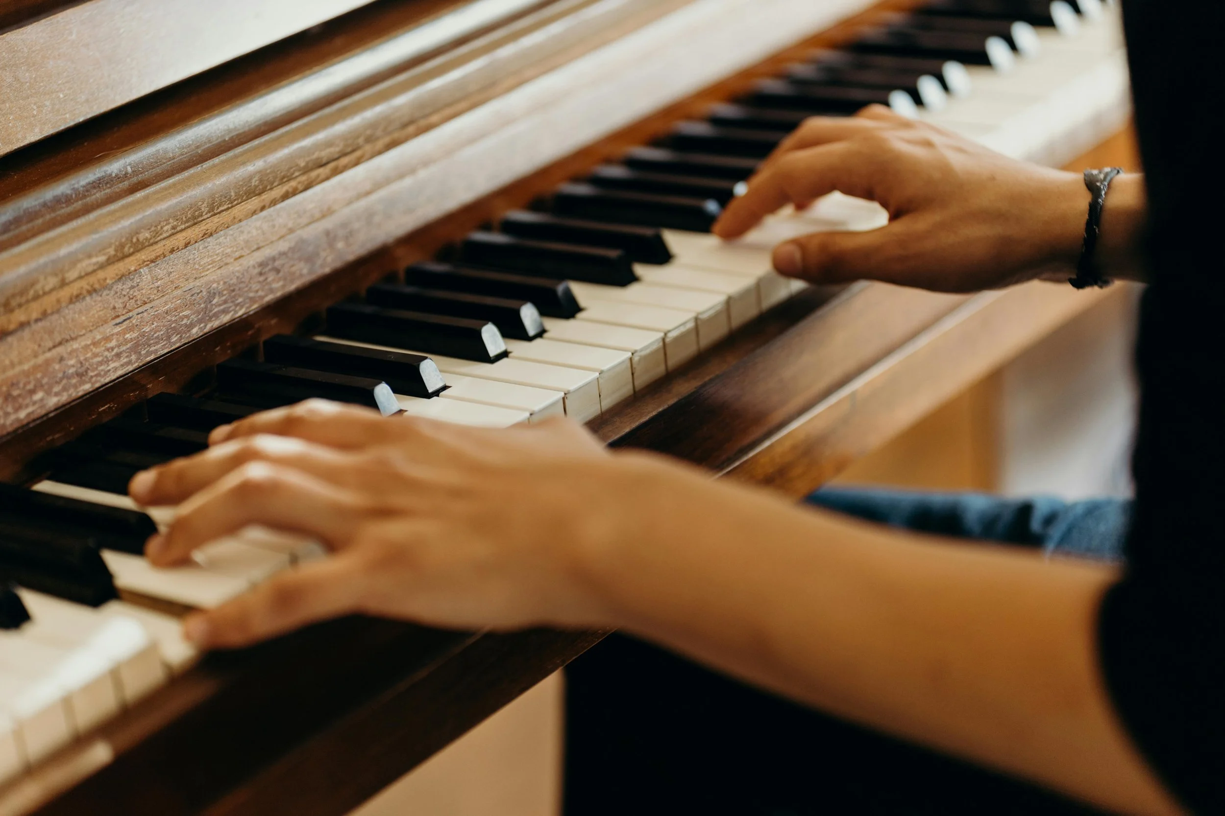 Hands playing an upright piano with wooden casing and black and white keys.