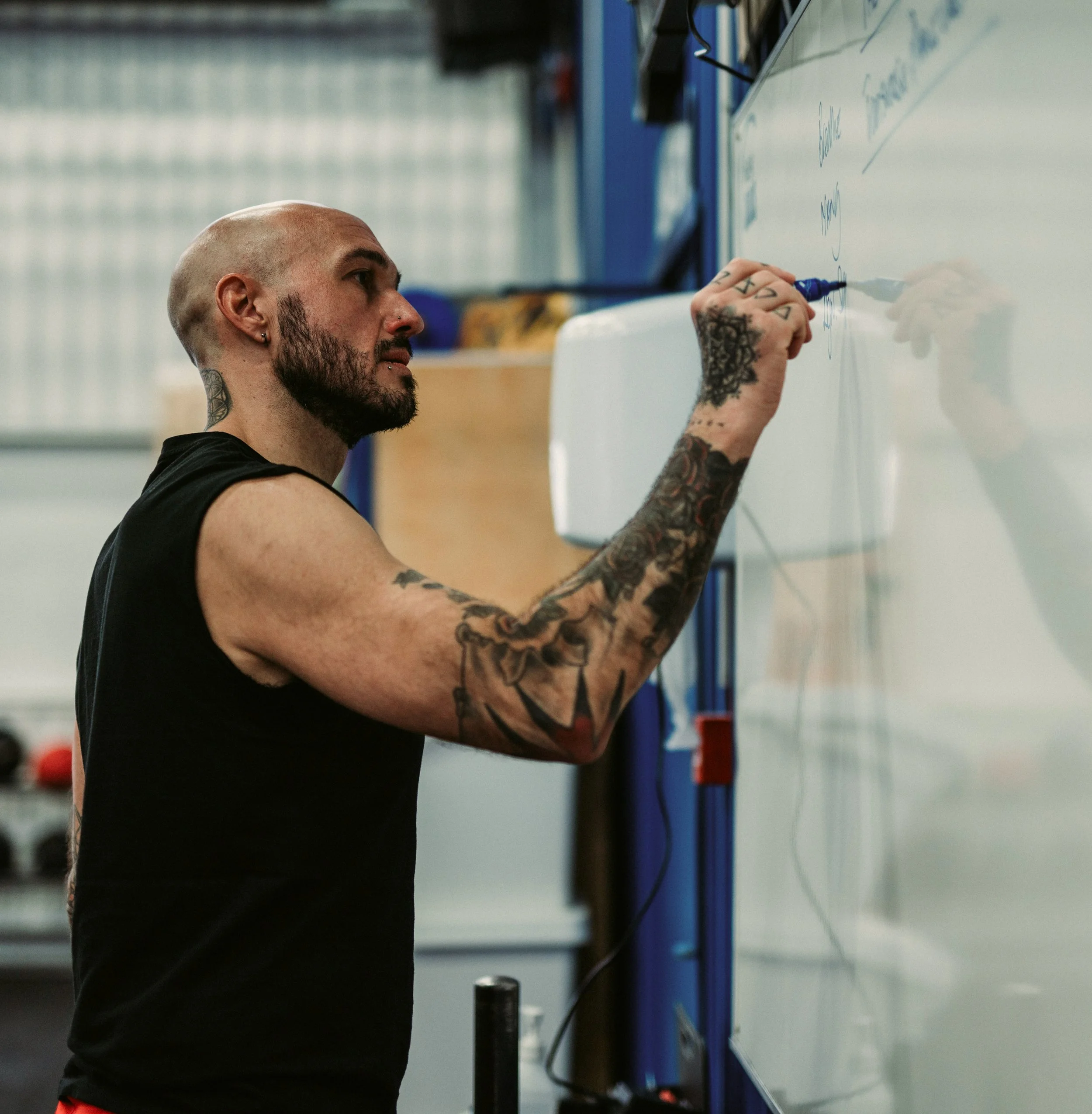 A man with tattoos writing on a whiteboard.