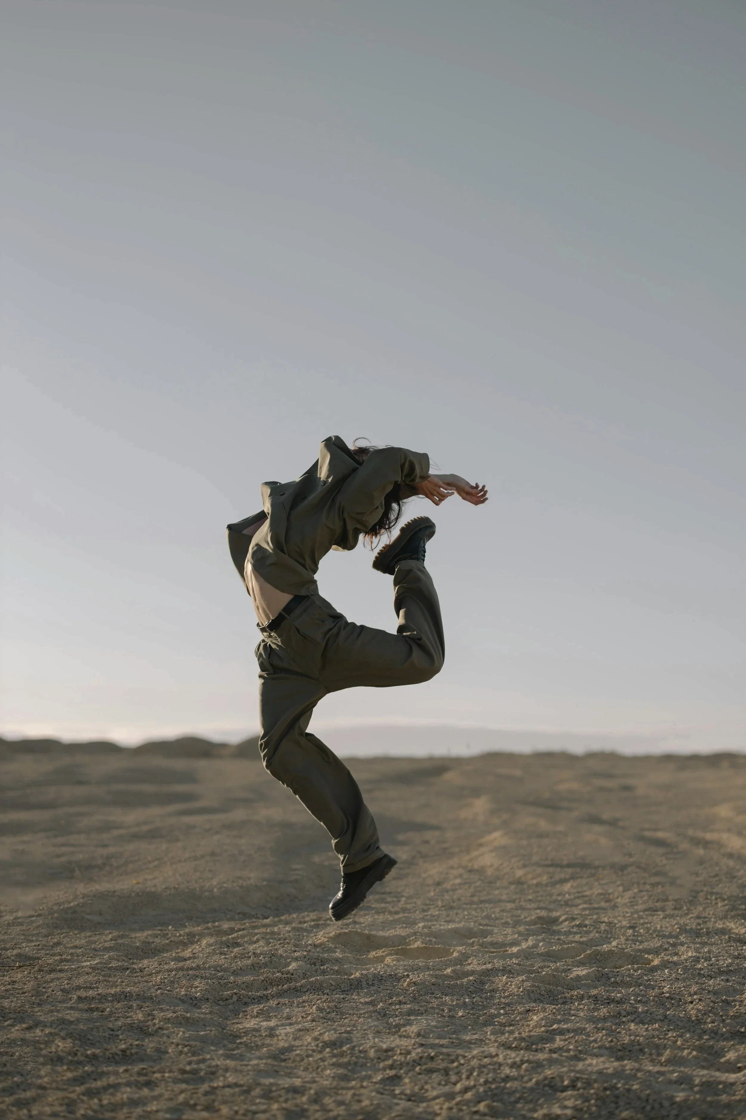 A person jumping in mid-air on a sandy, open landscape with a clear sky overhead.