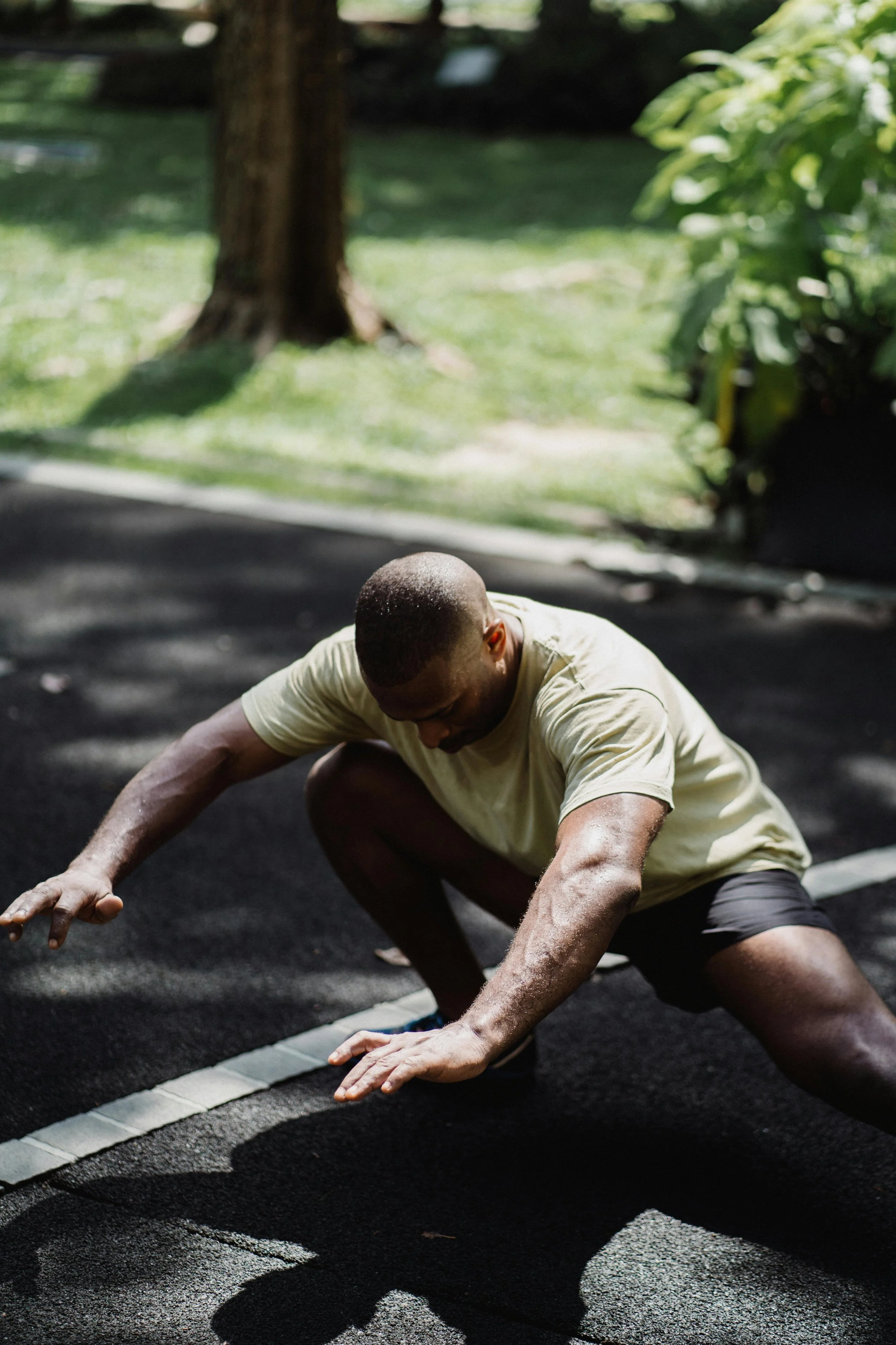 Man in a yellow shirt and black shorts doing a stretch on a black running track.