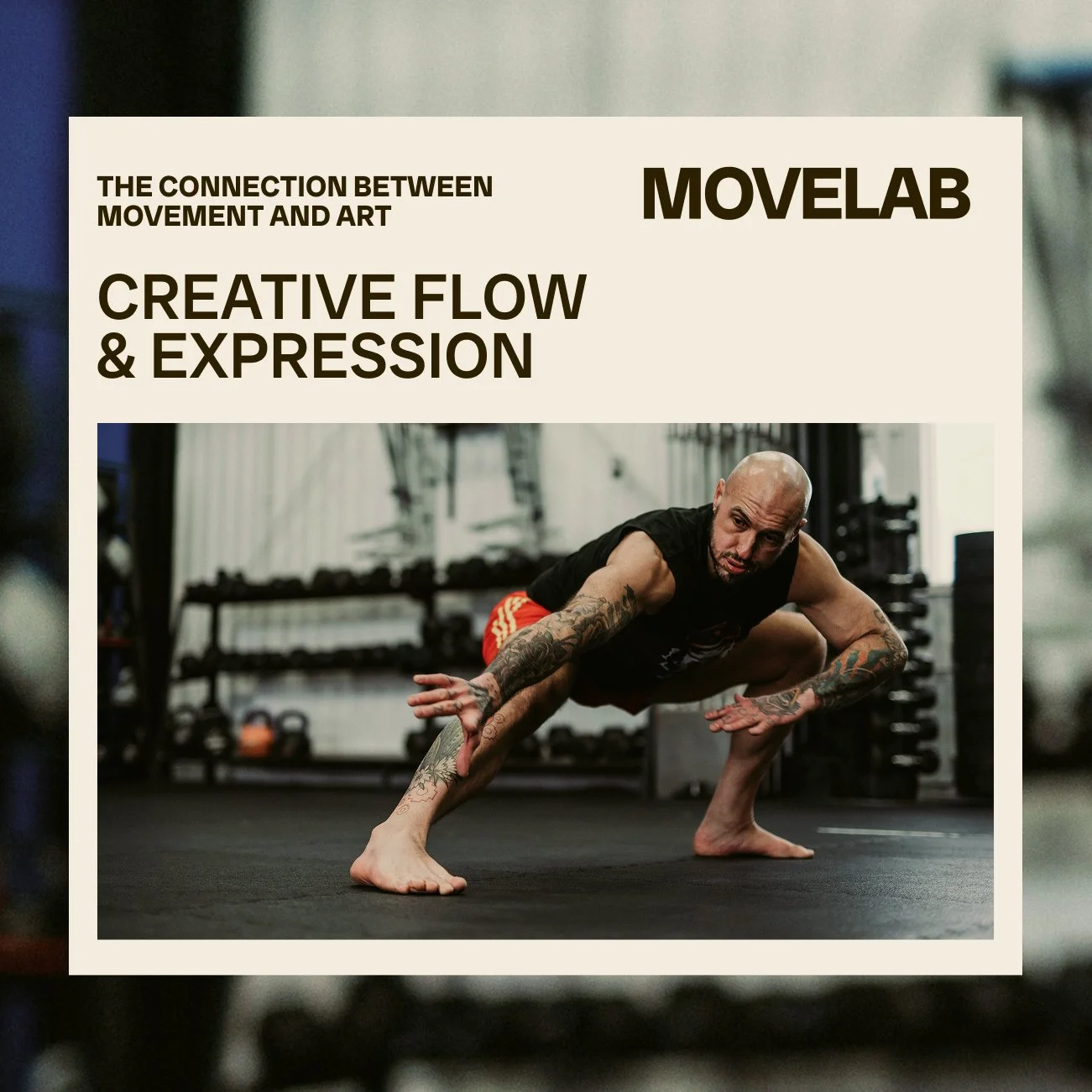 A man with tattoos doing a yoga pose on a black gym mat in a fitness studio with weights in the background.