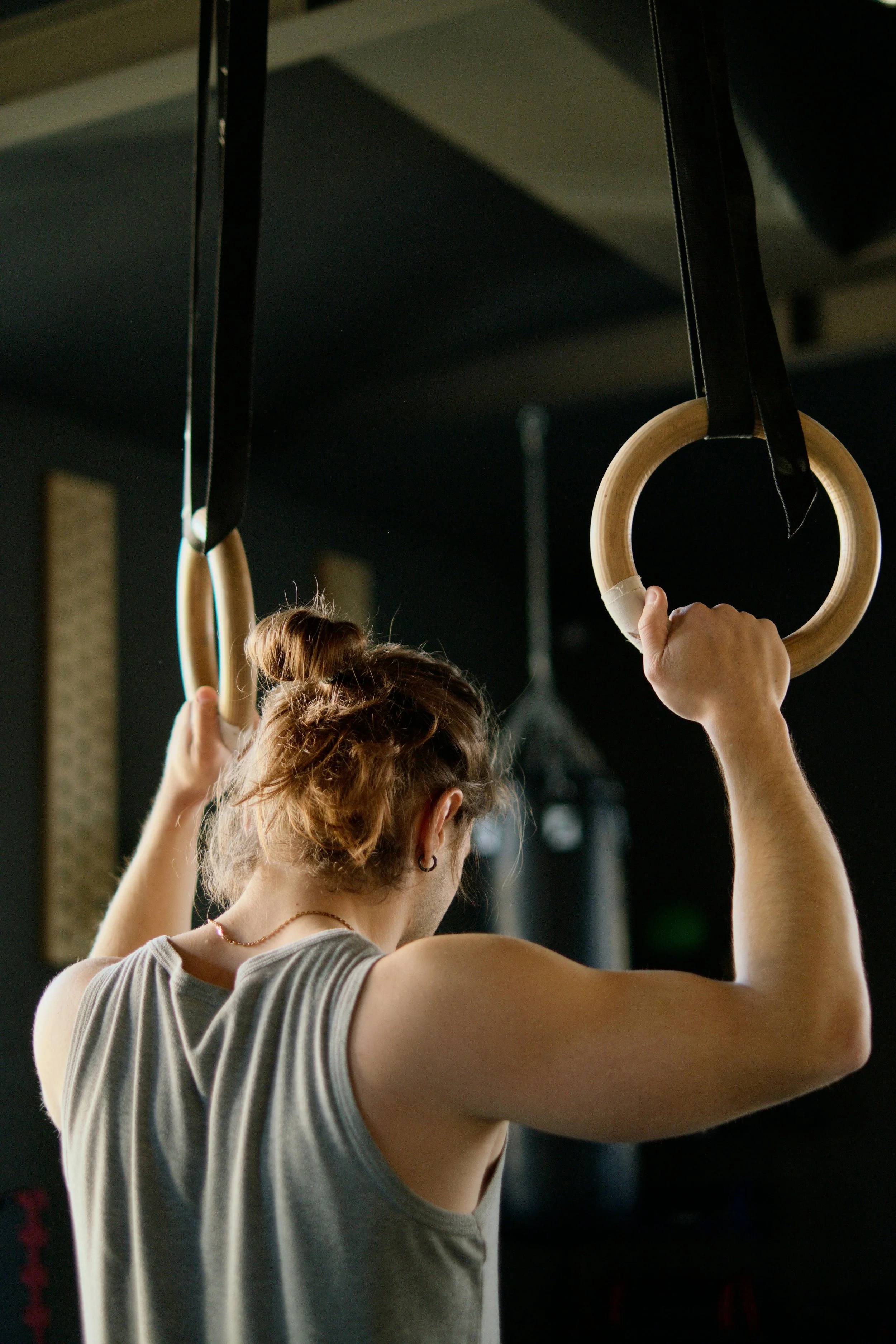 A person with braided hair wearing a sleeveless top holding gymnastic rings in a fitness gym.