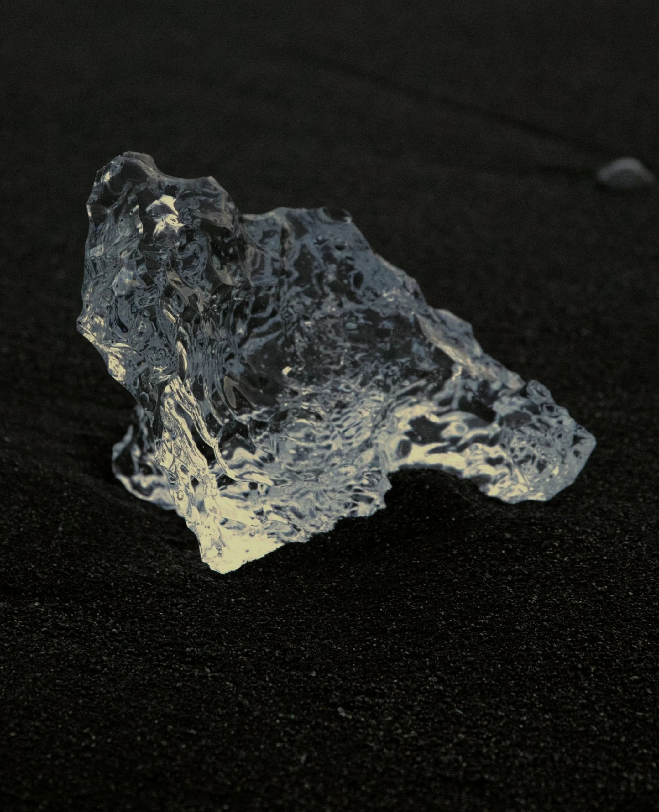 A clear, irregularly shaped piece of ice resting on a black surface.