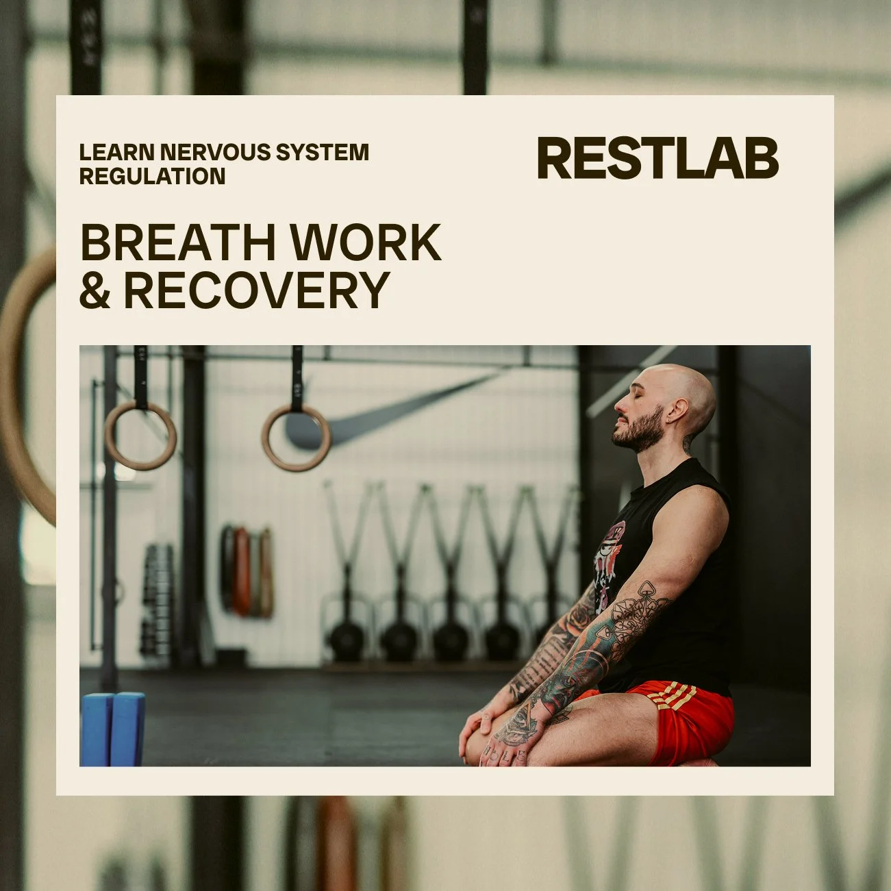 A man with tattoos practicing breathing exercises in a gym with gymnastics rings and resistance bands in the background.