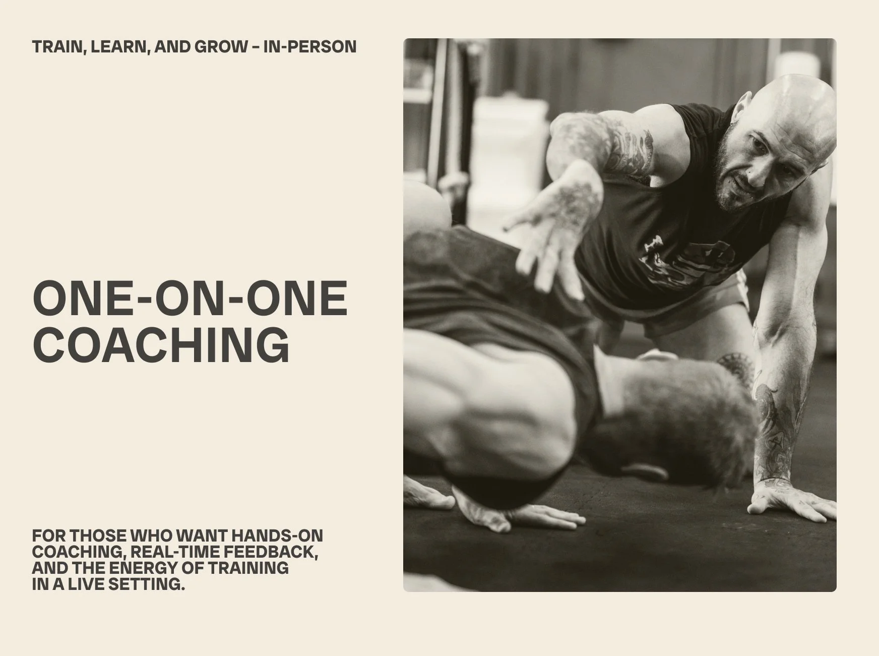 A man with tattoos coaching a person on one-on-one training session in a gym, both on the floor during an exercise.