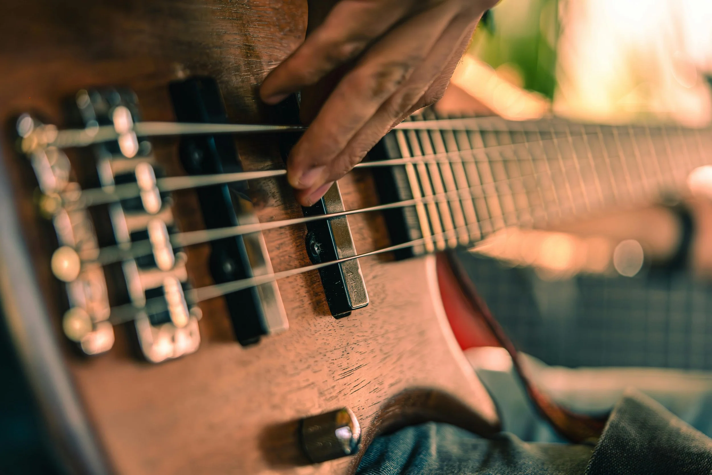 Close-up of a person's hand playing an acoustic guitar, focusing on the strings and fretboard with sunlight in the background.