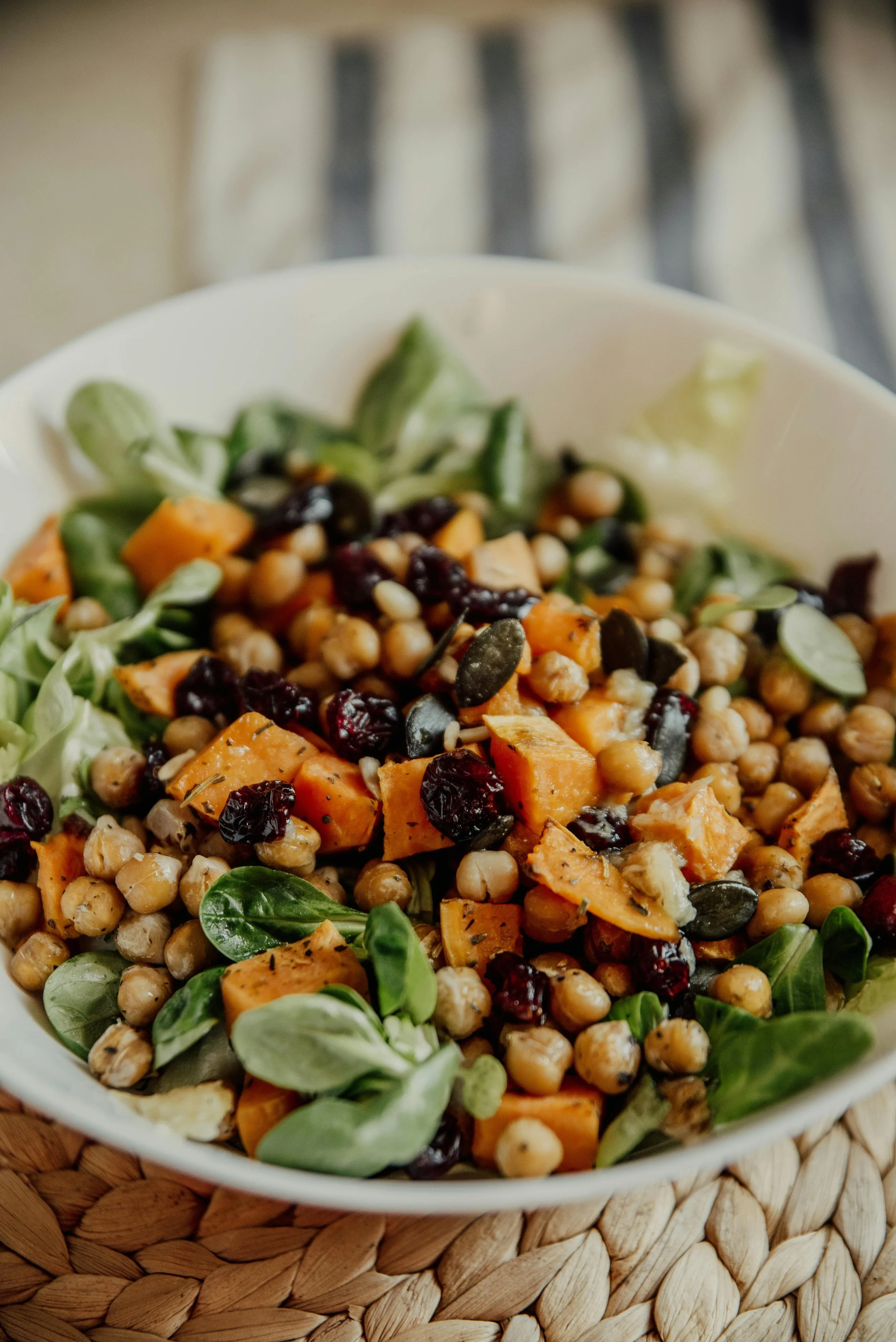 A bowl of chickpea, sweet potato, and cranberry salad with greens.