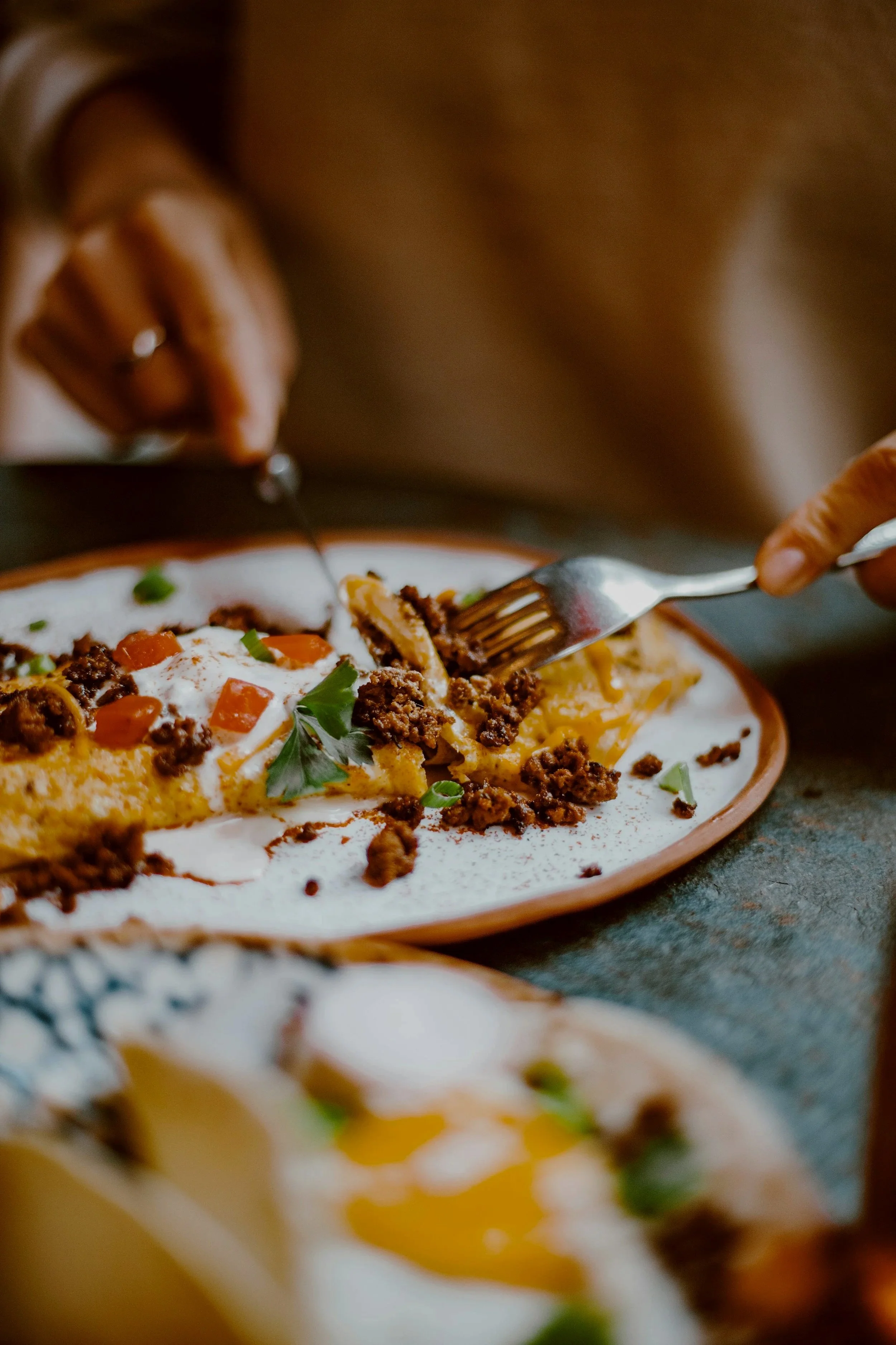 Person scooping beef, cheese, and tomato enchiladas with a fork on a plate.