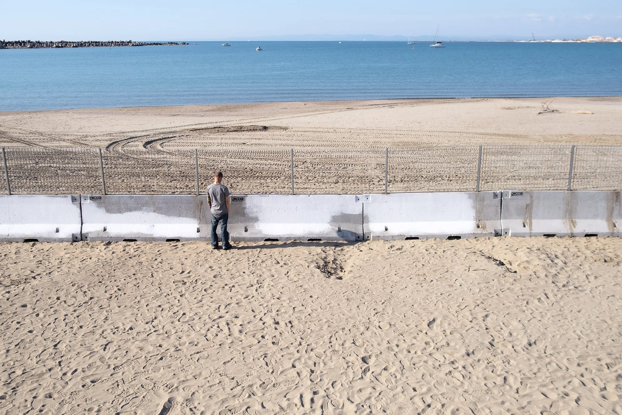 Fabio in front of the wall blocking access to the sea, 2024