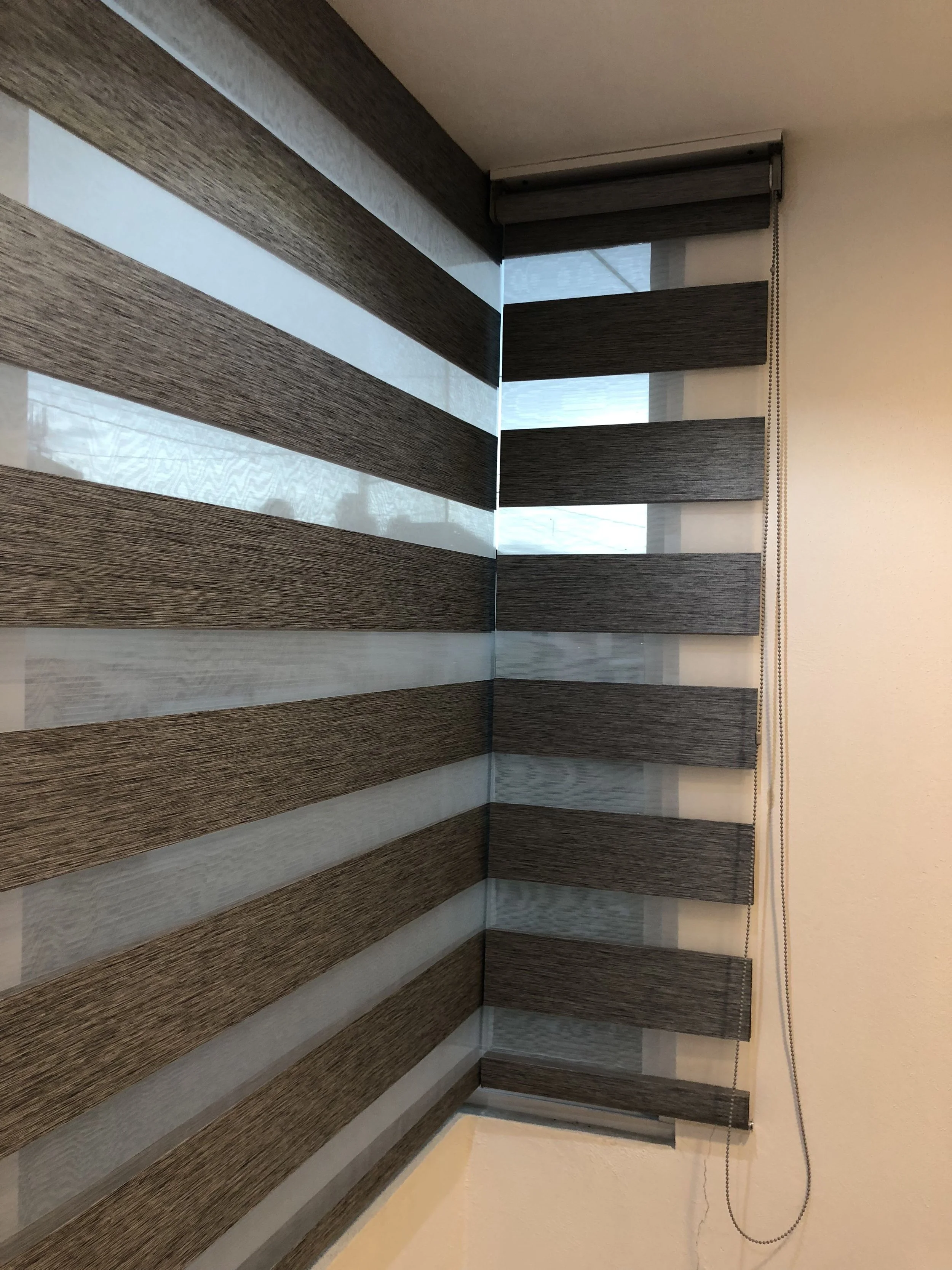 Persianas enrollables de tela marrón y blanca en una esquina de una habitación.