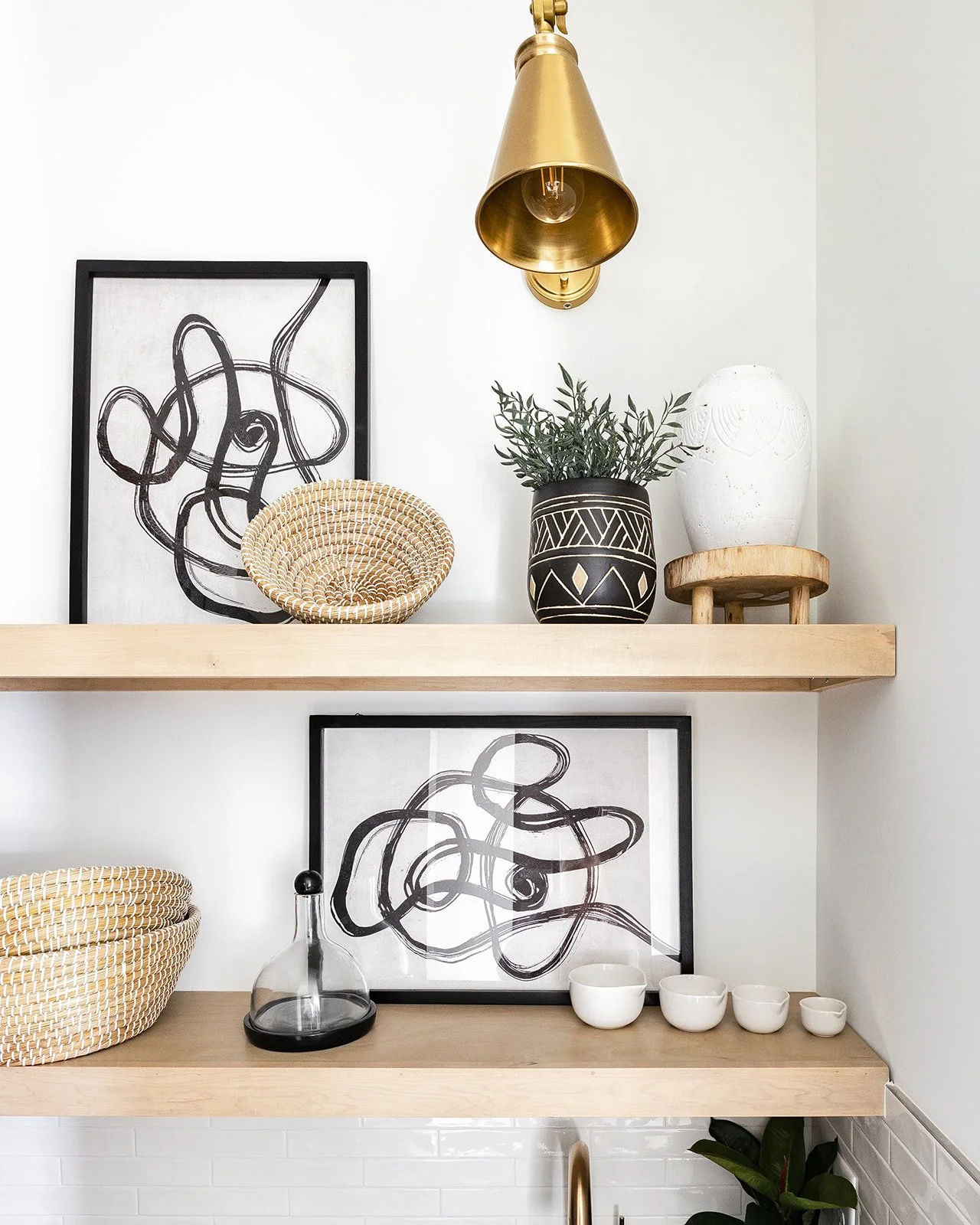 A modern shelf with a potted plant, vases, and paintings.
