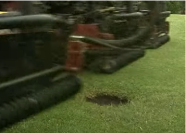 A lawn mower with a patch of grass torn up underneath it on a grassy lawn.
