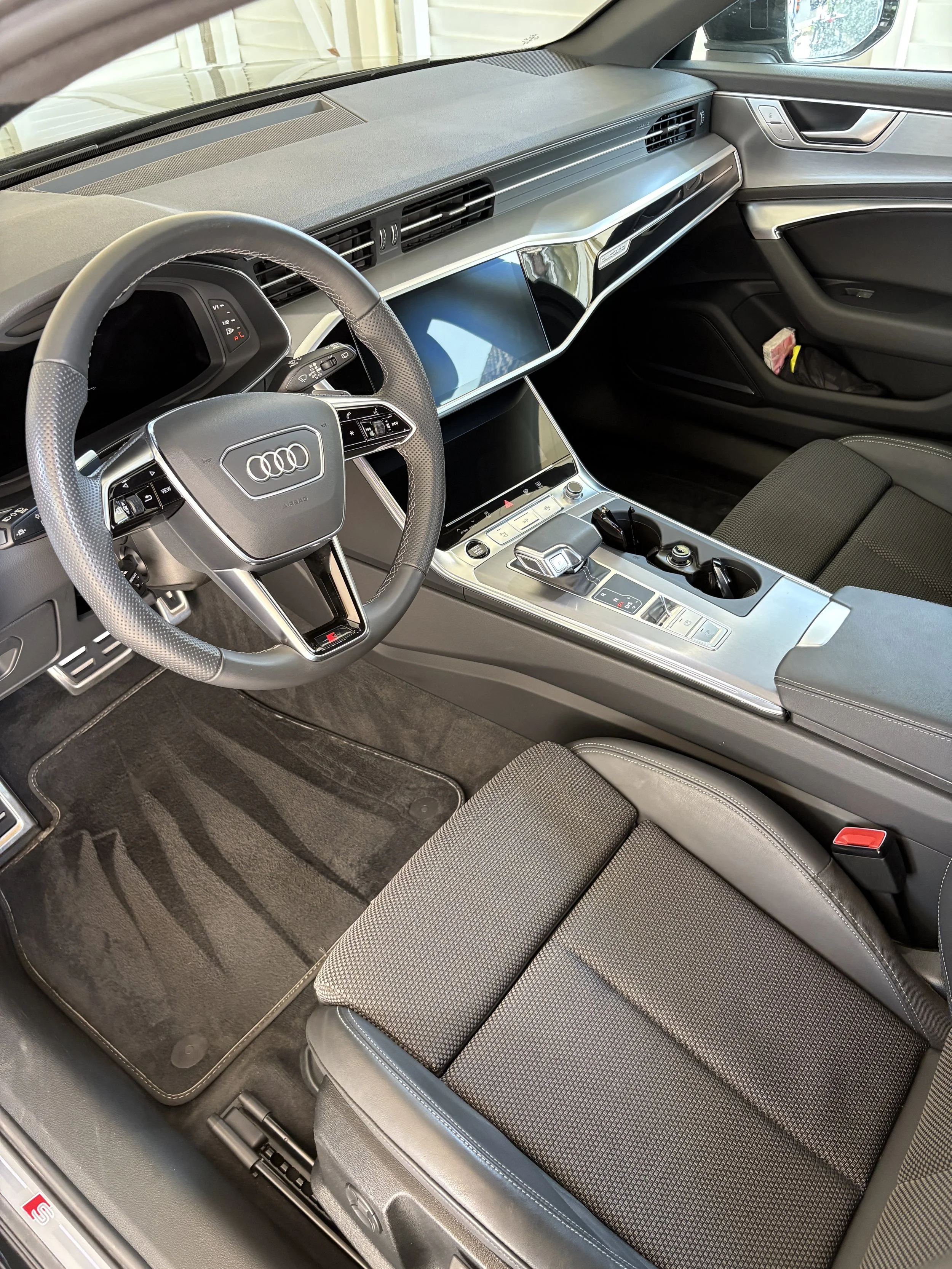 Innenansicht eines Autos, geprägt von modernem Armaturenbrett, großem Touchscreen, Lenkrad mit multiple Bedienungselementen, Automatikgetriebe, dunkler Innenausstattung, Sitz mit Stoffbezug.