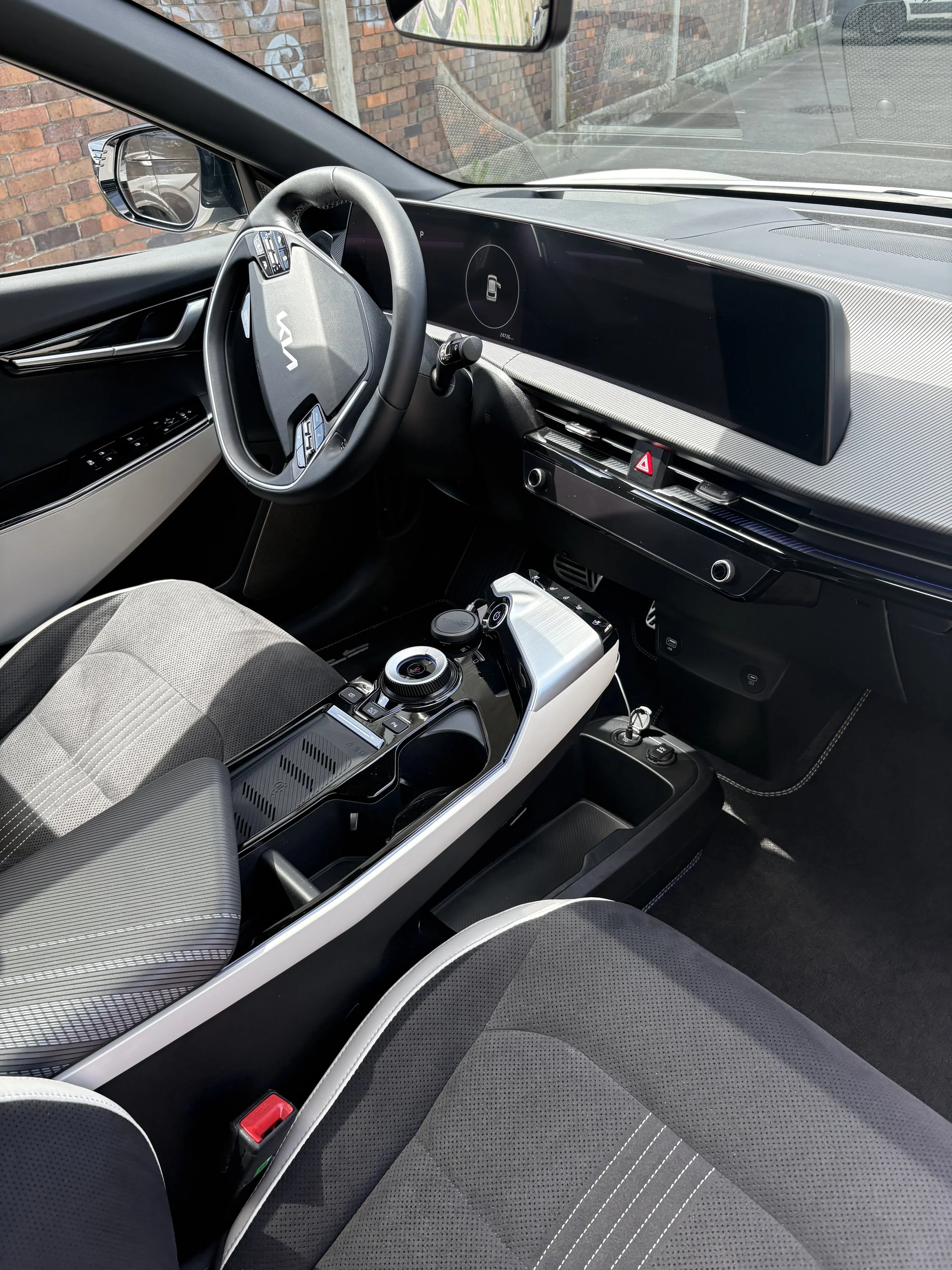 Innenansicht eines modernen Fahrzeugs mit digitalem Armaturenbrett, Lederlenkrad und schwarzem Armaturenbrett. Der Sitz ist grau mit weißen Nähten. Das Bild zeigt den Fahrerbereich eines Elektroautos.