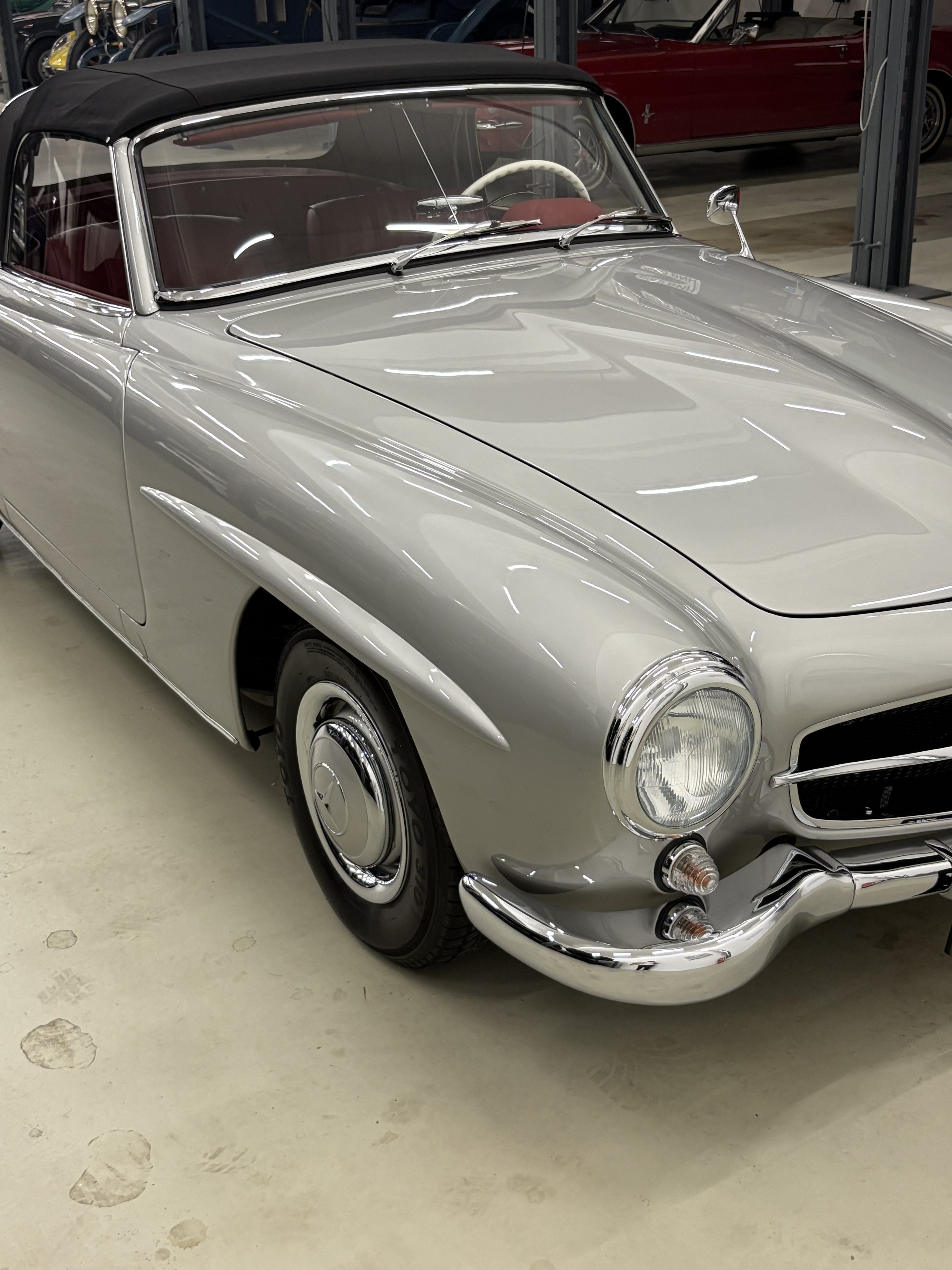 Ein silberner Oldtimer-Cabrio mit schwarzem Verdeck, vermutlich ein Mercedes-Benz 300SL, abgestellt in einer Garage.