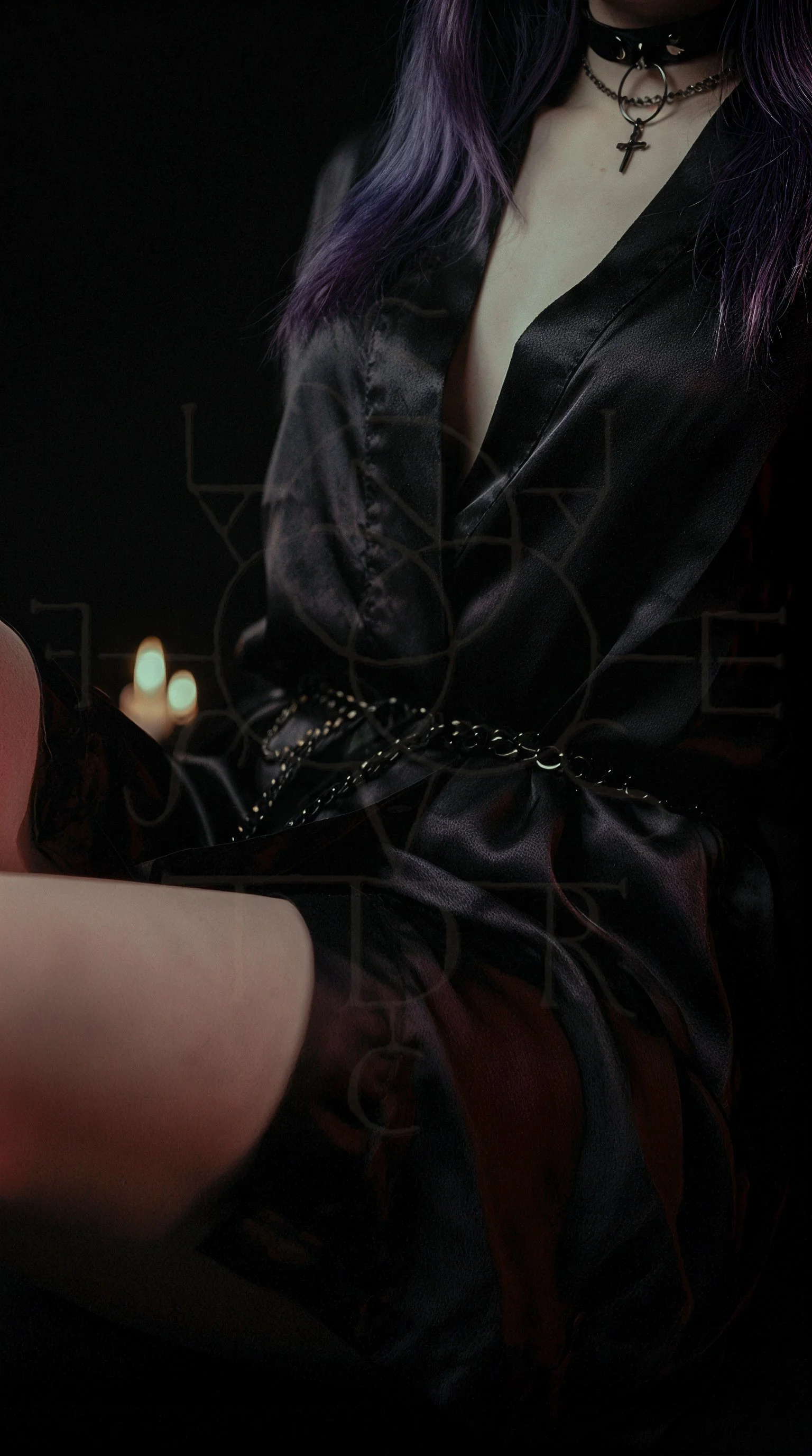 Close-up of a woman wearing a black satin robe, choker with a ring and cross pendant, and purple hair, with a blurred background.