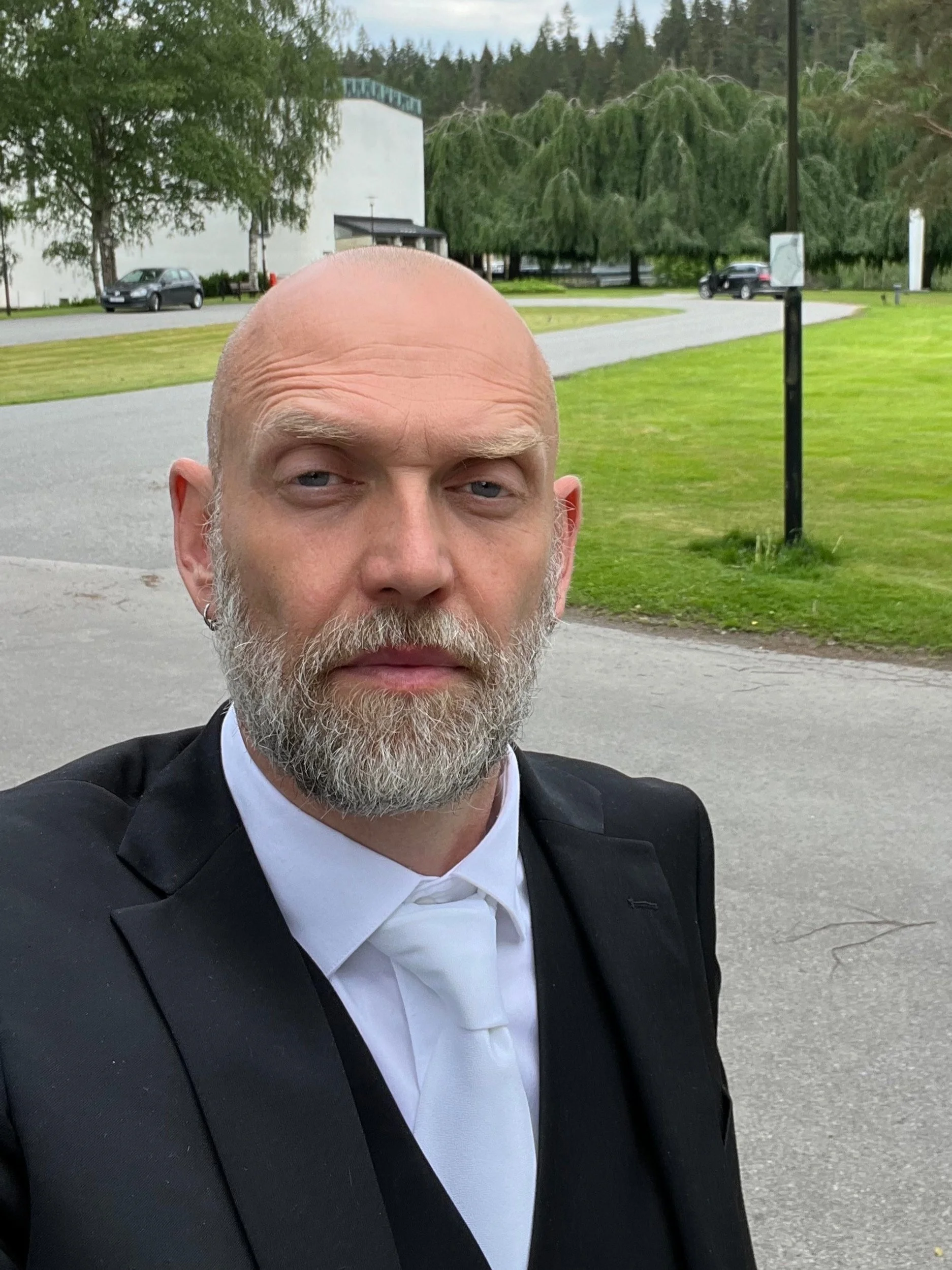 Henrik i kostym och slips utomhus med grönska i bakgrunden.