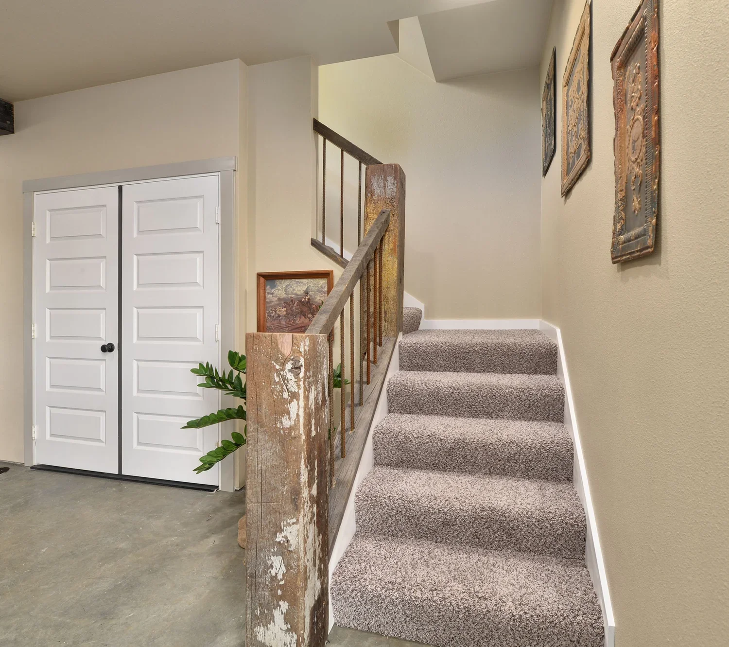Carpeted staircase in a Montana home with rustic wood newel post, white double doors, framed art, and neutral walls, showing a practical western entryway design that blends rustic interior design with modern updates.