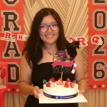 A photo of a girl holding a cake in front of a grad party poster
