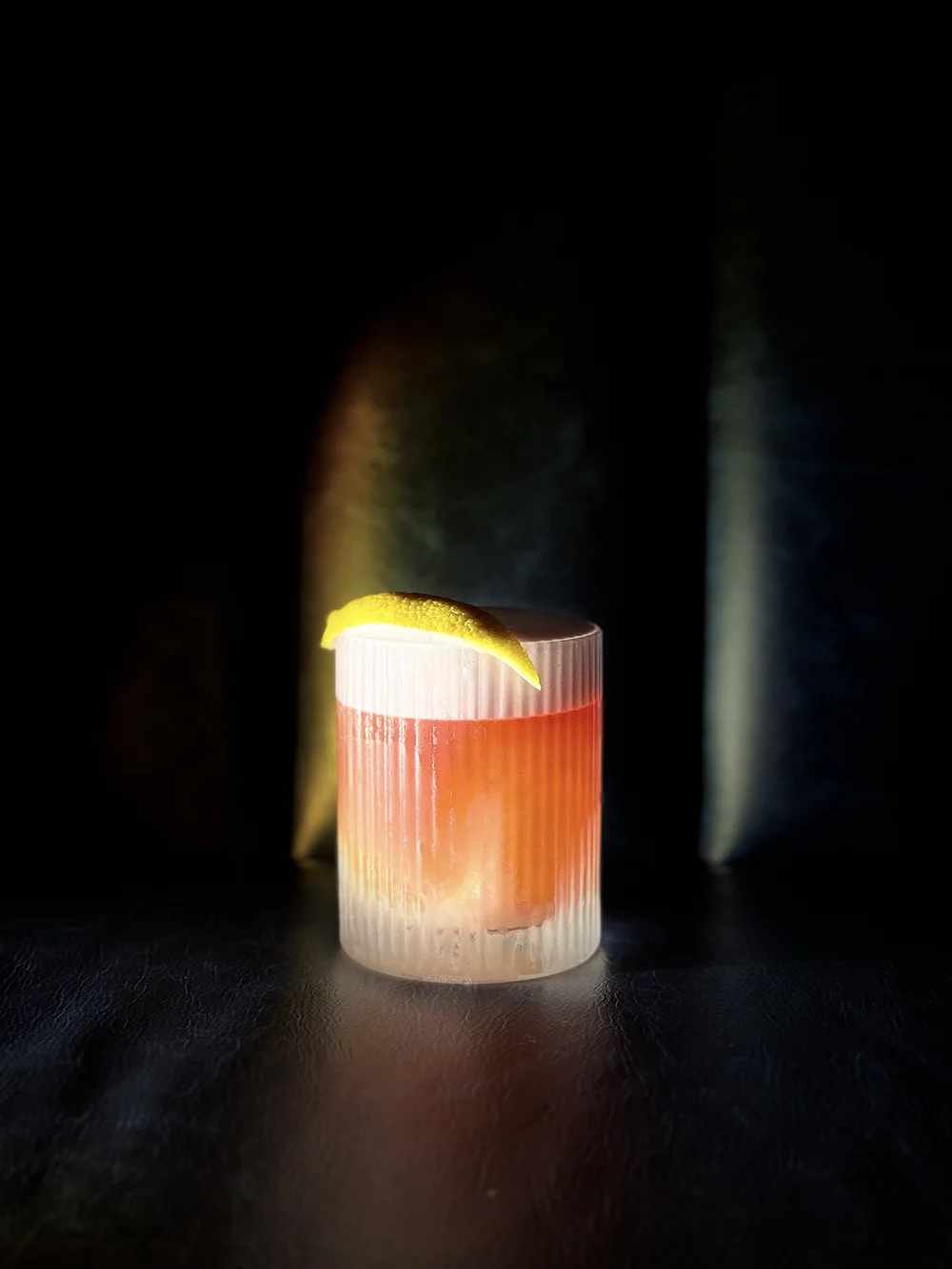 A cocktail in a textured glass with lemon garnish