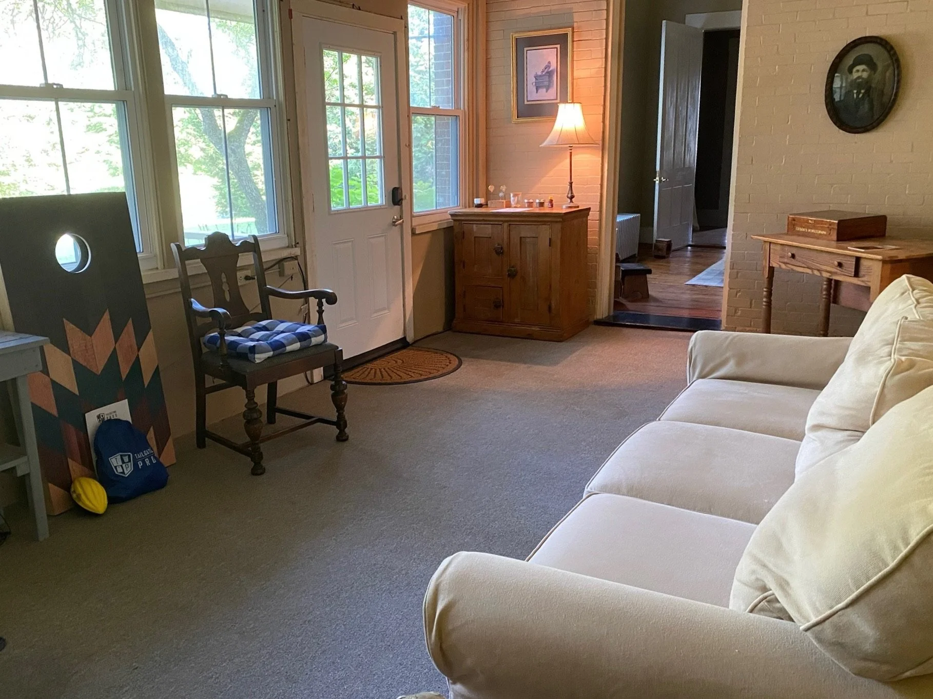 Living room with a beige sofa, wooden furniture, a lamp, and large windows showing a green outdoor scene.