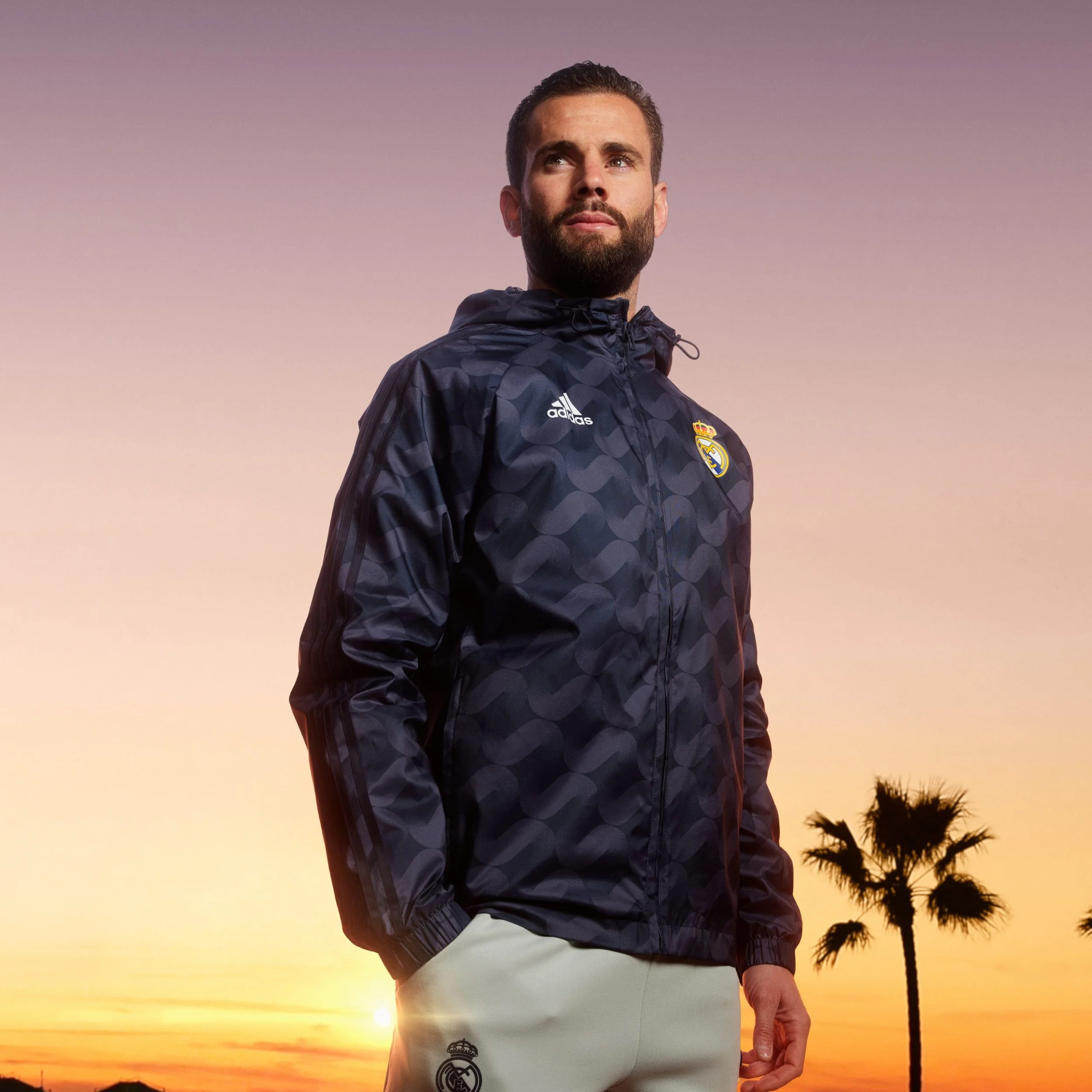 Hombre con chaqueta deportiva de Real Madrid Away durante atardecer, con palmera en el fondo.