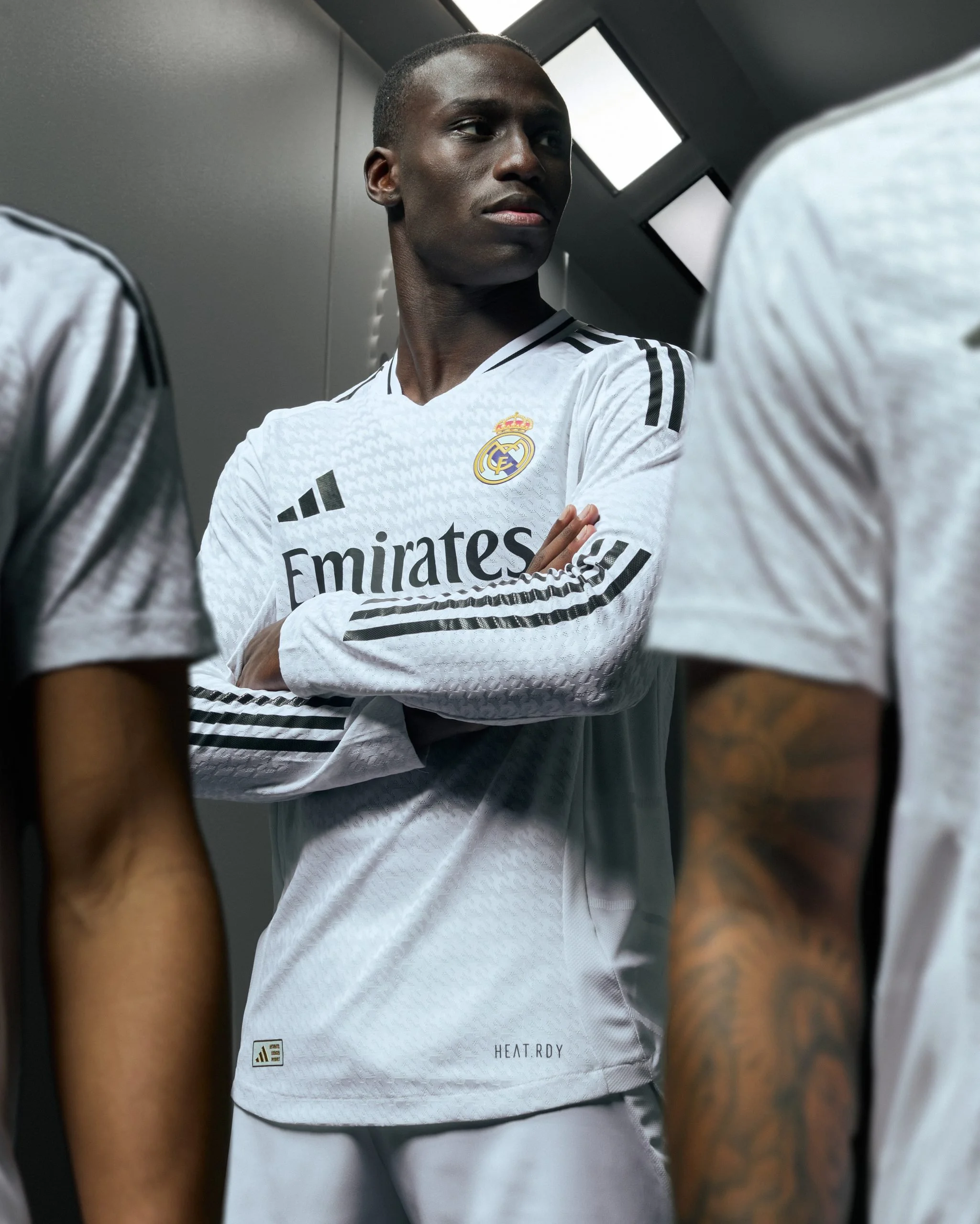 Un jugador de fútbol con uniforme adidas del Real Madrid, en un vestidor, parece estar hablando con sus compañeros.