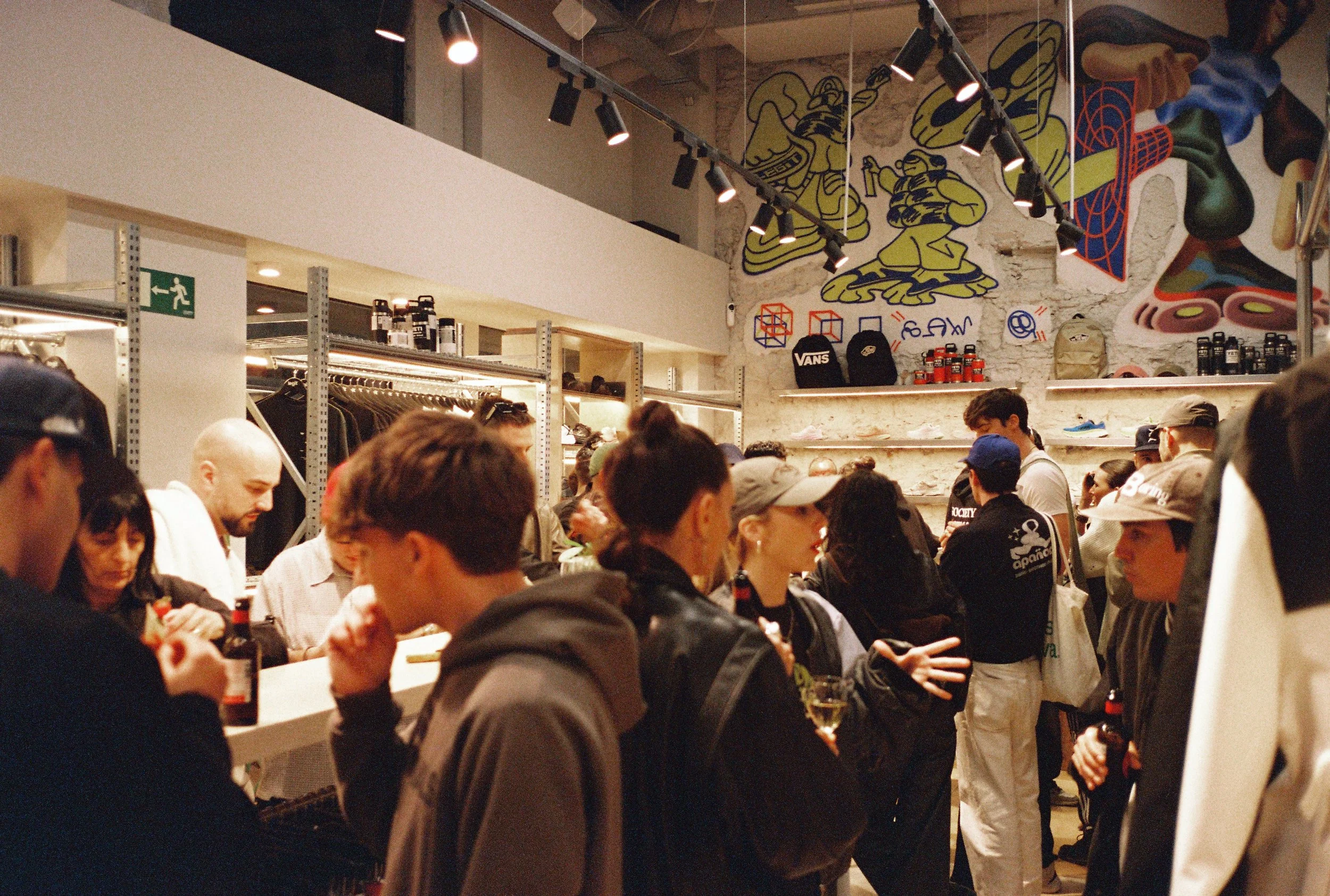 Interior de una tienda de ropa con muchas personas comprando y un mural colorido en la pared . Apertura local Legit Barcelona -