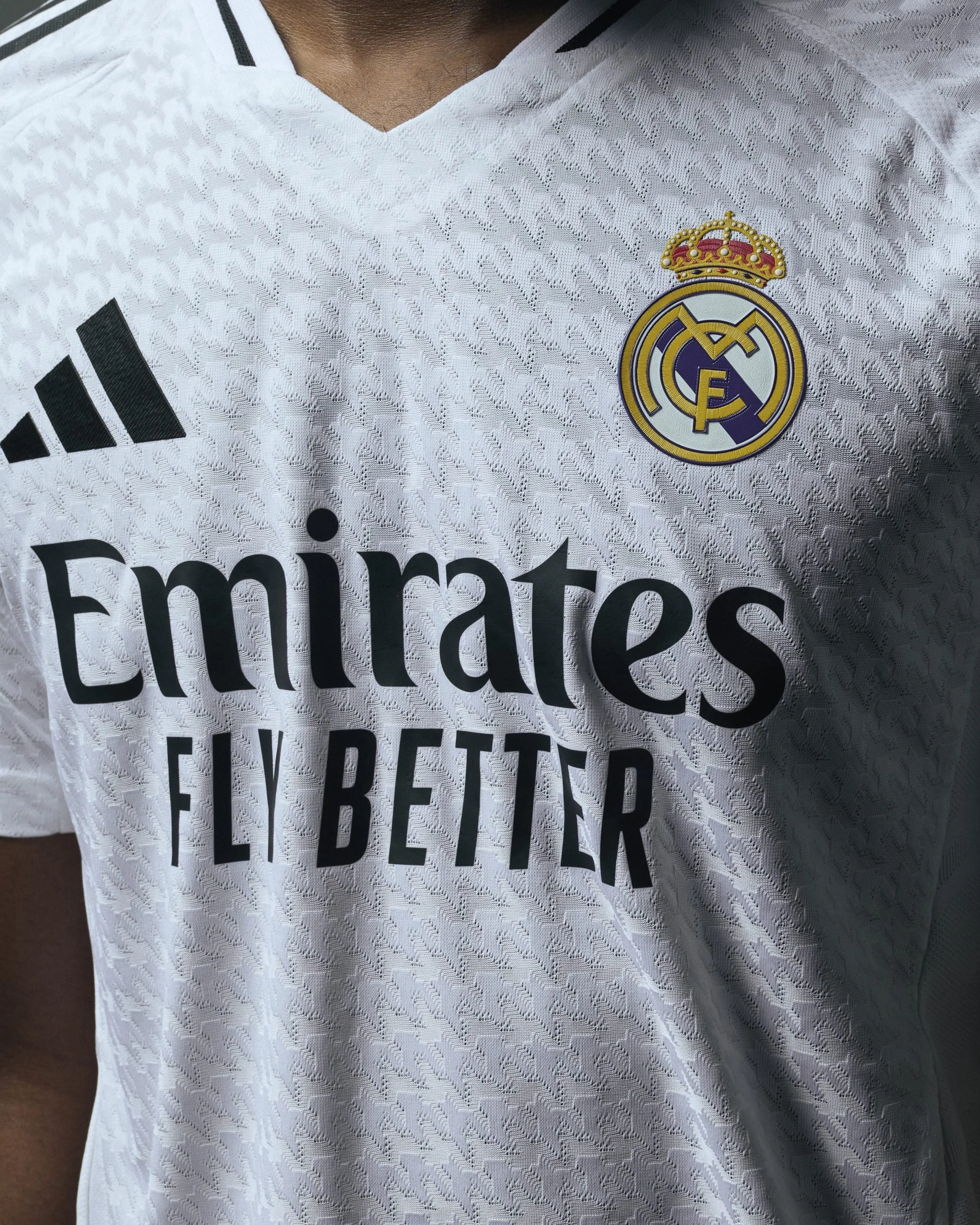 Camiseta blanca de fútbol con el escudo del Real Madrid, logo de Adidas y patrocinador Emirates en español.