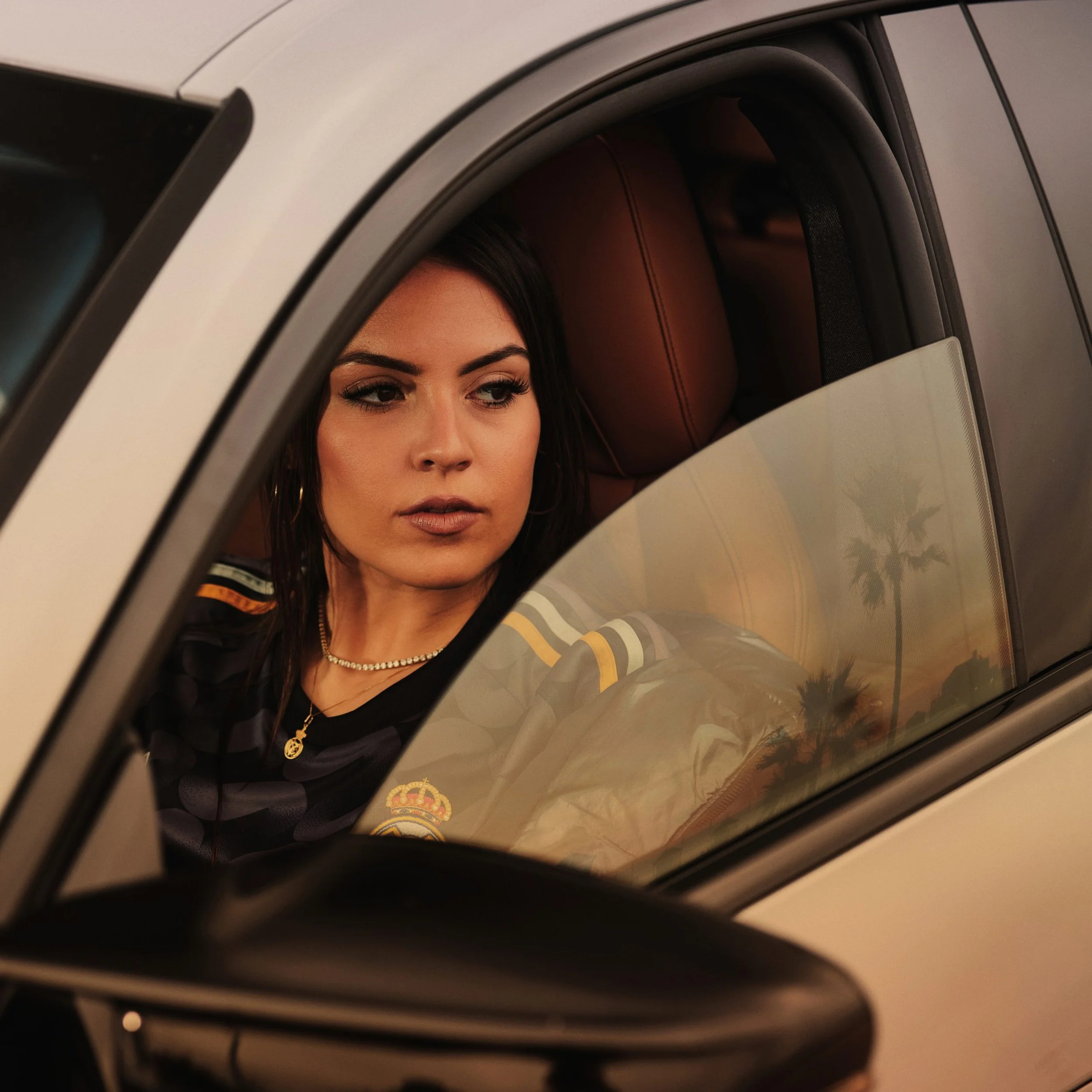 Joven mujer mira por la ventana de un coche, con fondo de palmeras y atardecer
