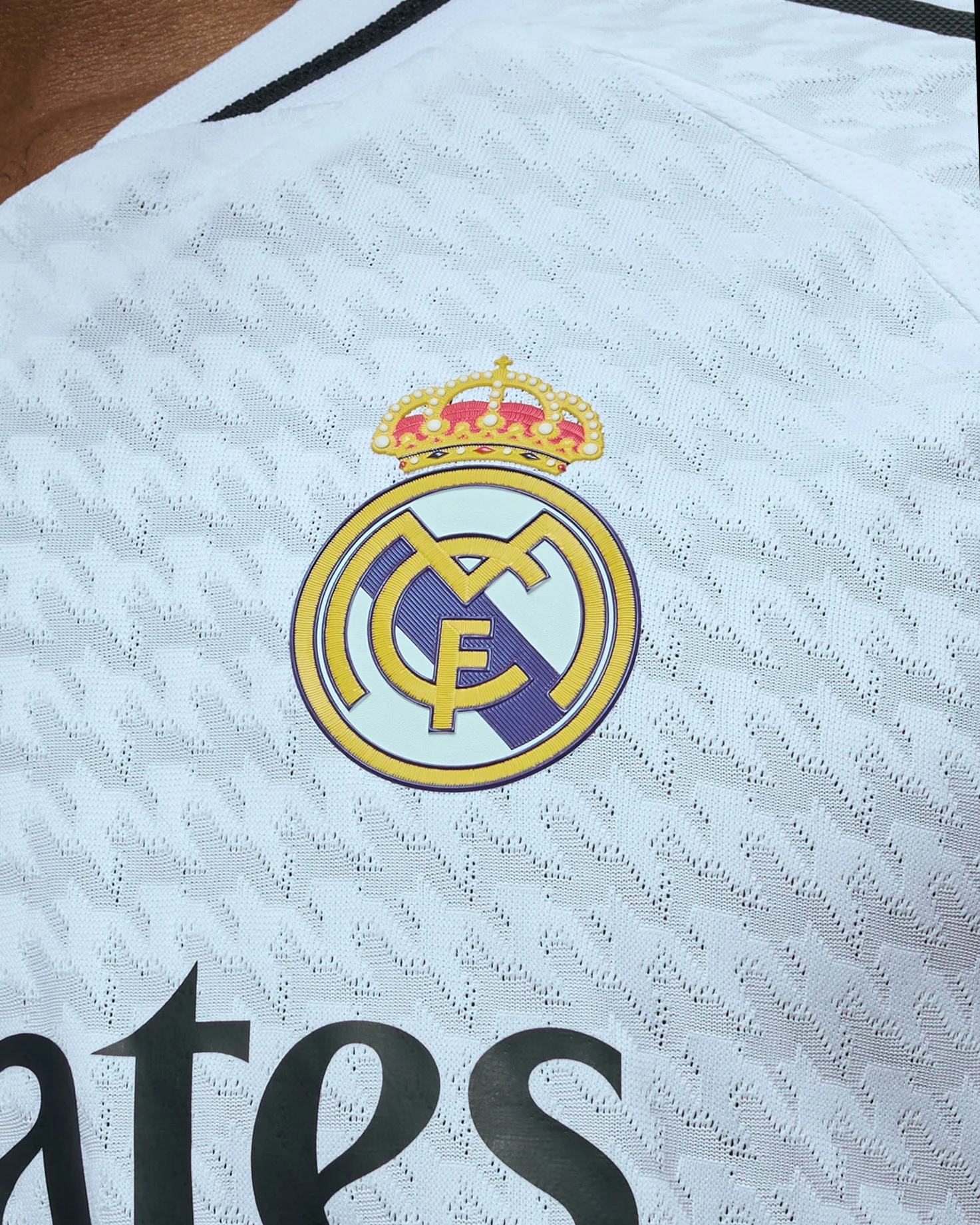 Logotipo del equipo de fútbol Real Madrid en una camiseta adidas blanca con detalles en negro.