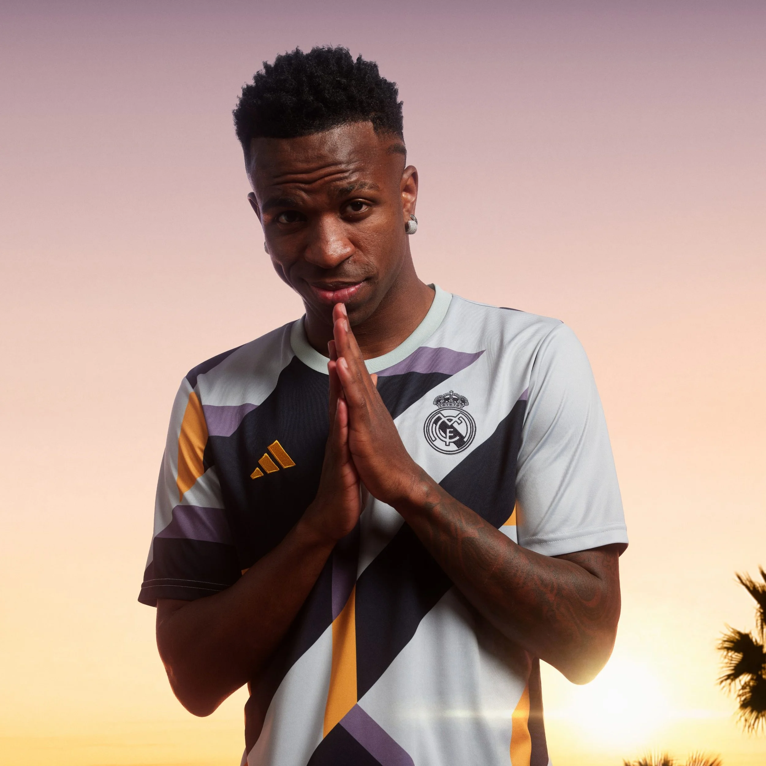 Hombre con camiseta del Real Madrid, haciendo una señal de oración con las manos, en un atardecer