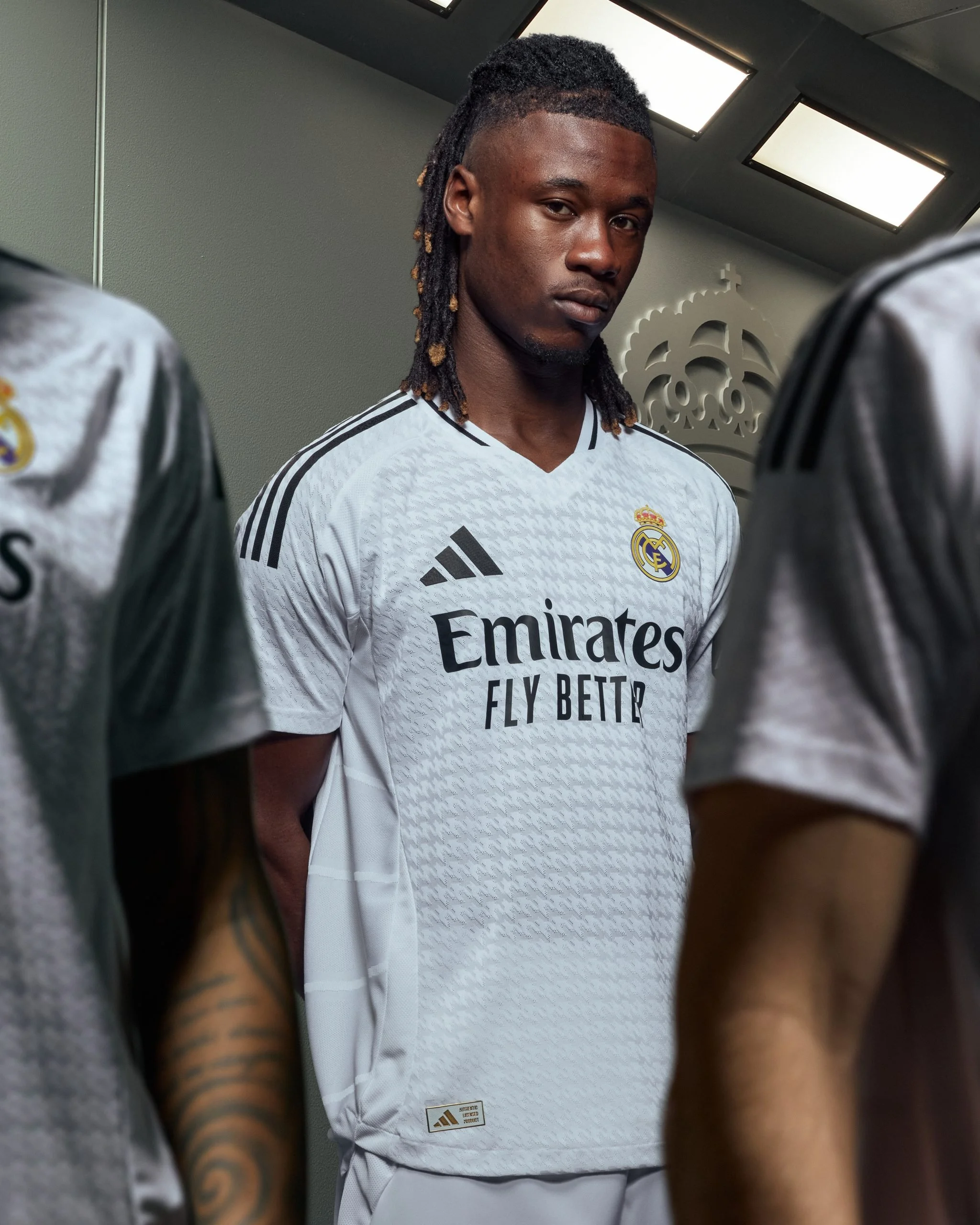 Un jugador del Real Madrid en vestimenta de fútbol adidas, rodeado de compañeros, en un vestuario.