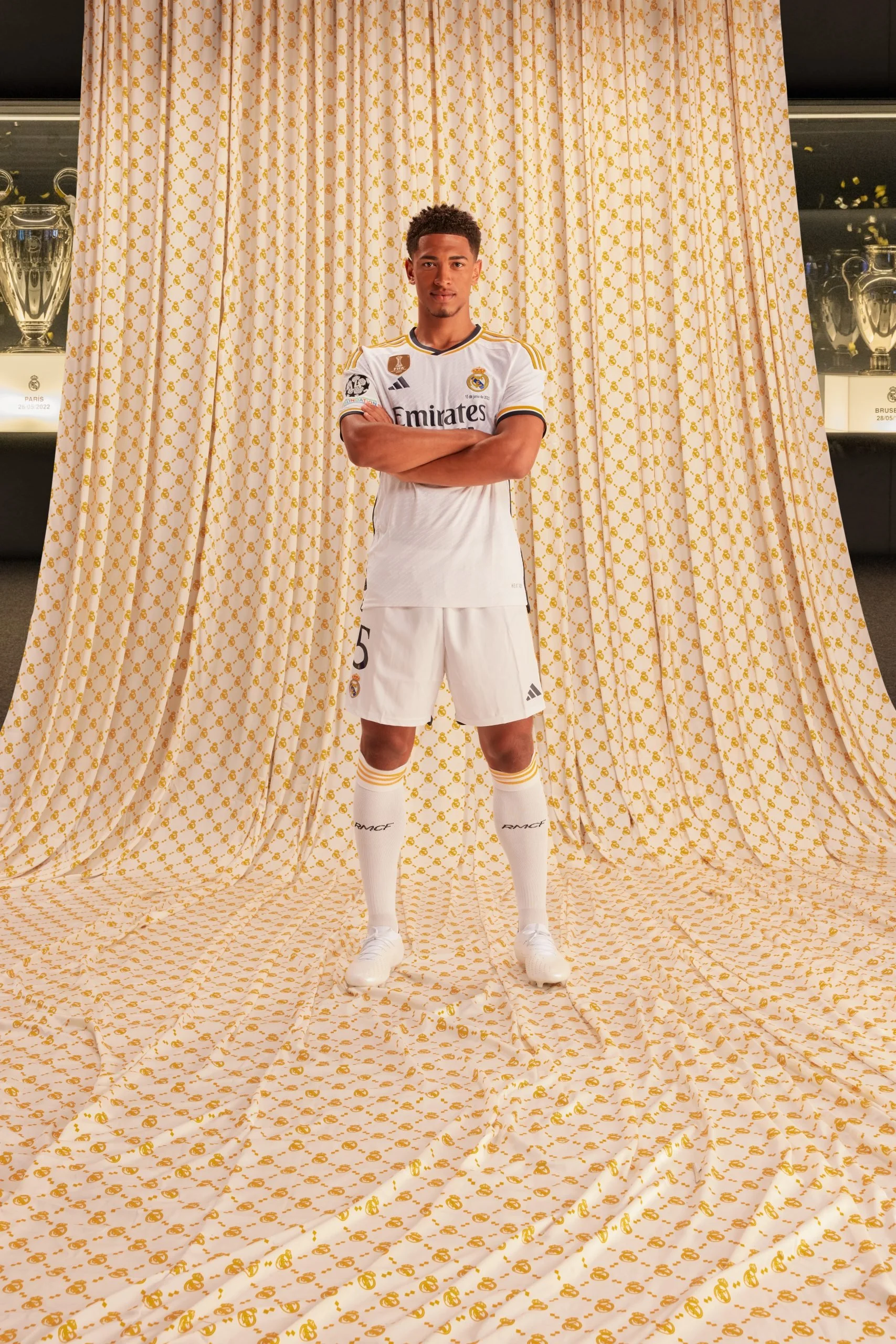 Jugador de fútbol en uniforme adidas Real Madrid en campaña amor incondicional posando con fondos y cortinas de tela con patrón dorado.