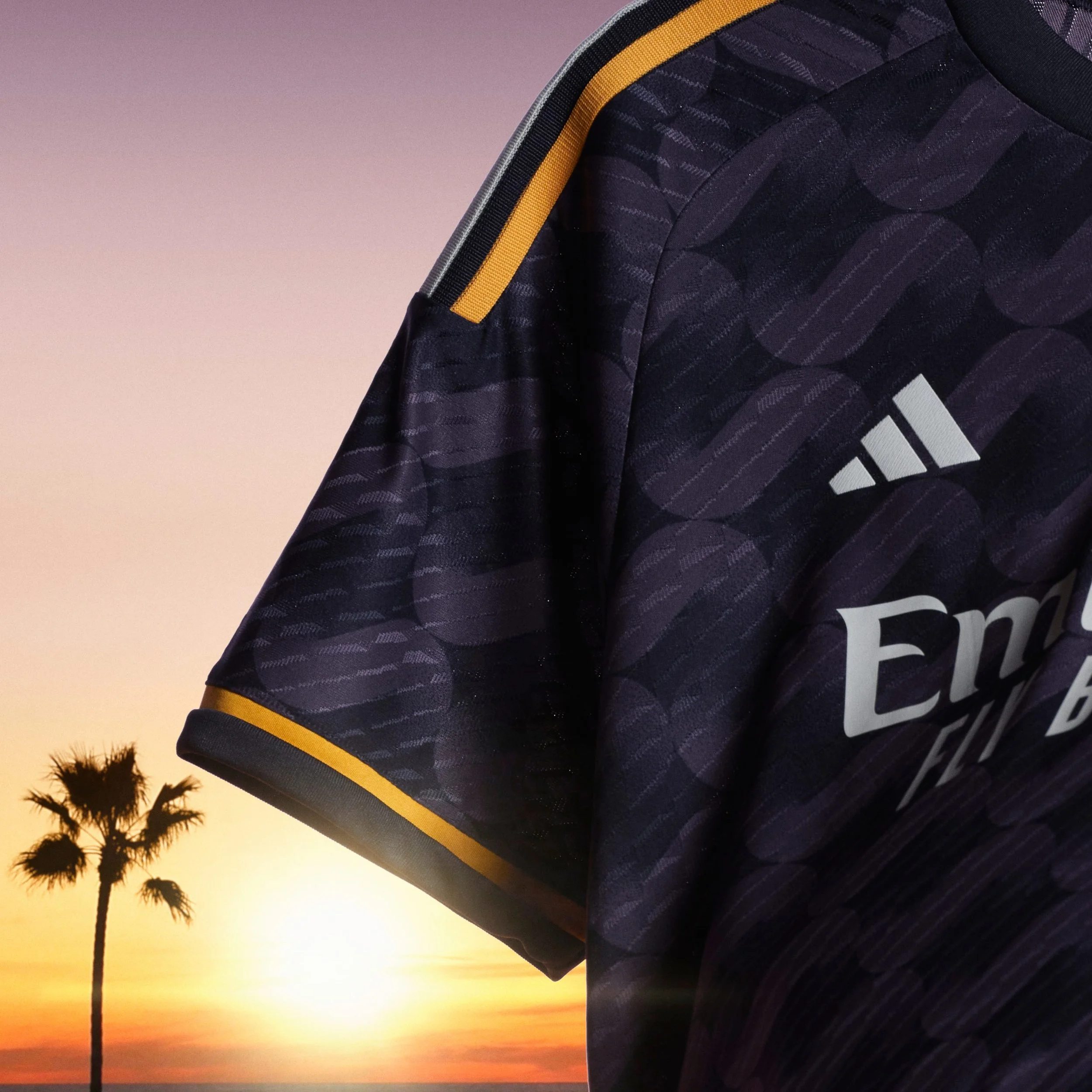 Camiseta deportiva de color morado con detalles en amarillo y logo de Adidas, con un fondo de atardecer en la playa con palmeras.